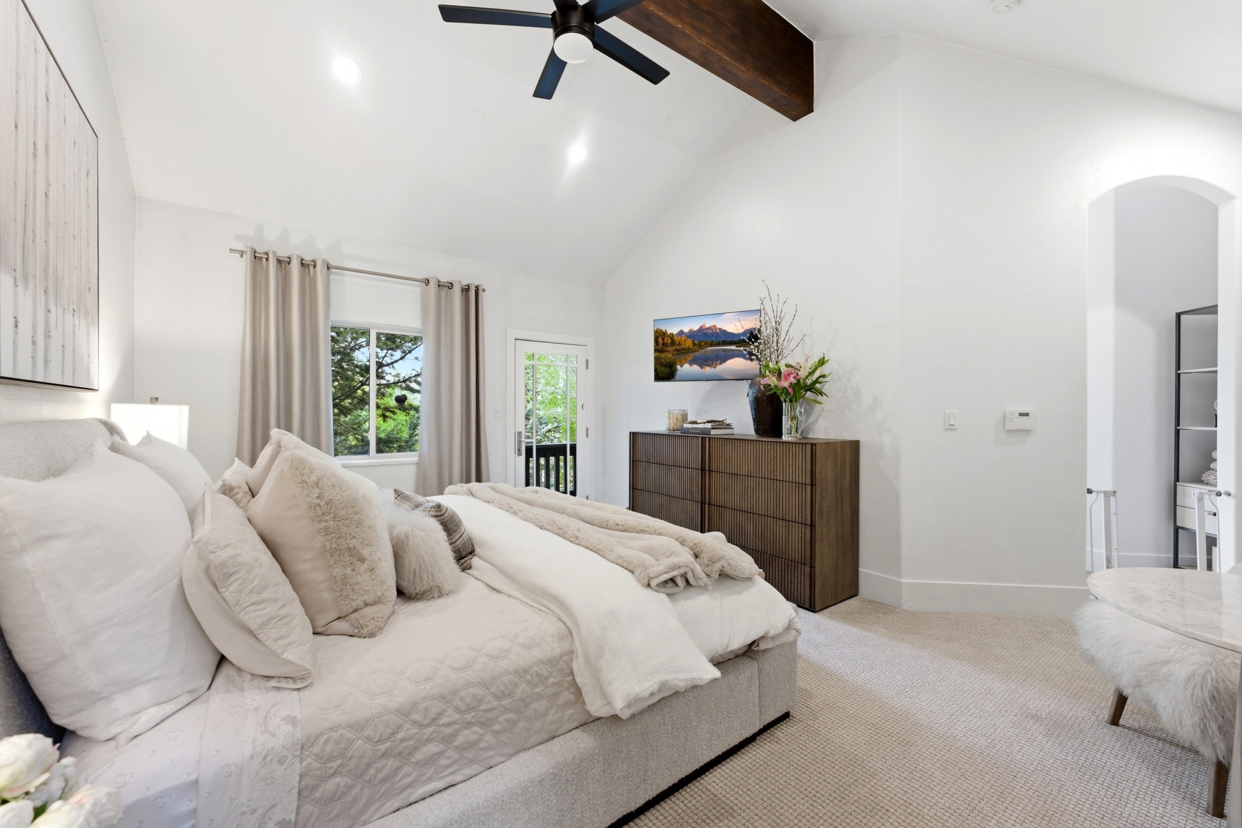 Vaulted ceiling with an exposed wood beam, contemporary ceiling fan, recessed lighting, and a glass-paneled door opening to an exterior area