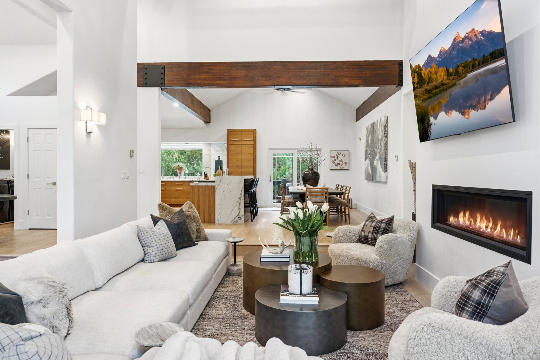Living room featuring vaulted ceilings with exposed wood beams, a linear gas fireplace, and wood-finish flooring