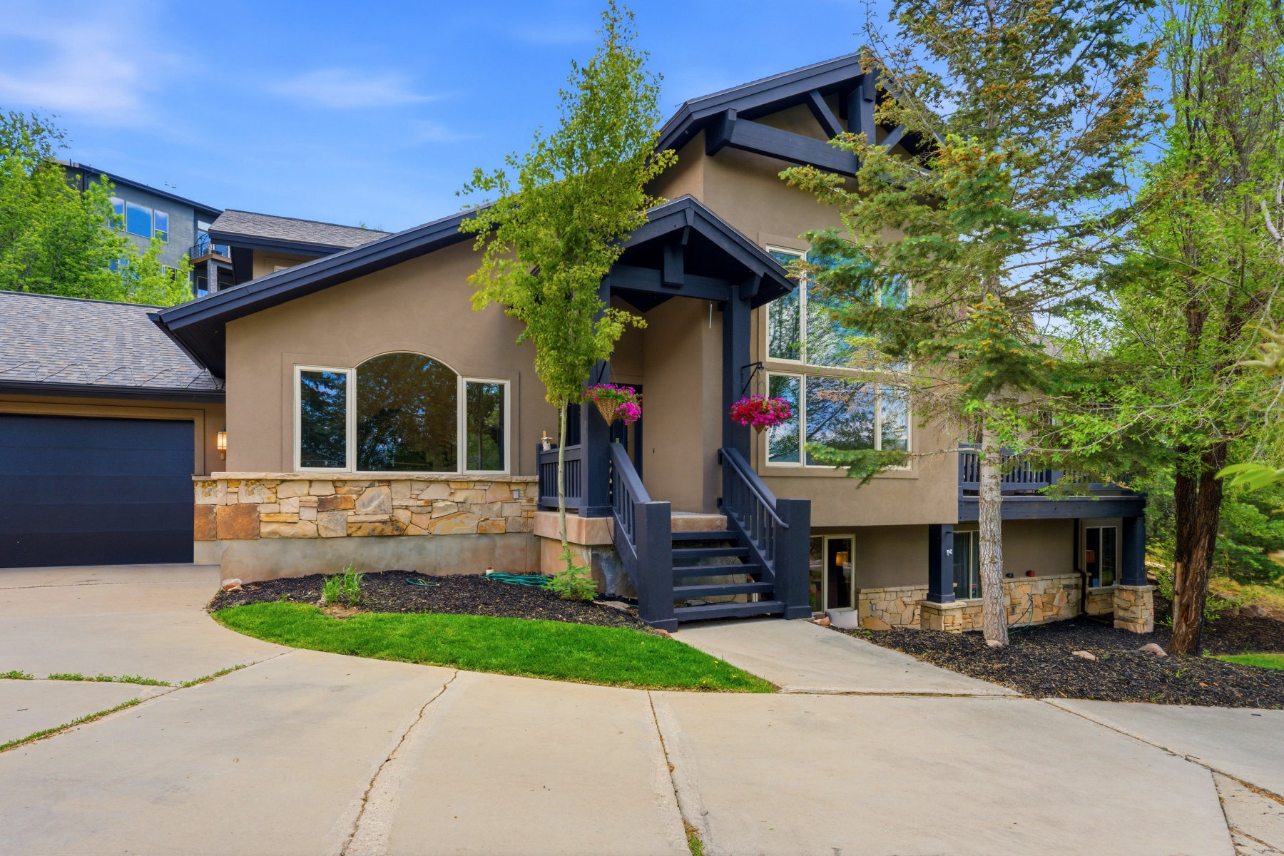 Stucco and stone facade home featuring a prominent two-car garage with a dark door, a multi-pane arched window, and large picture windows