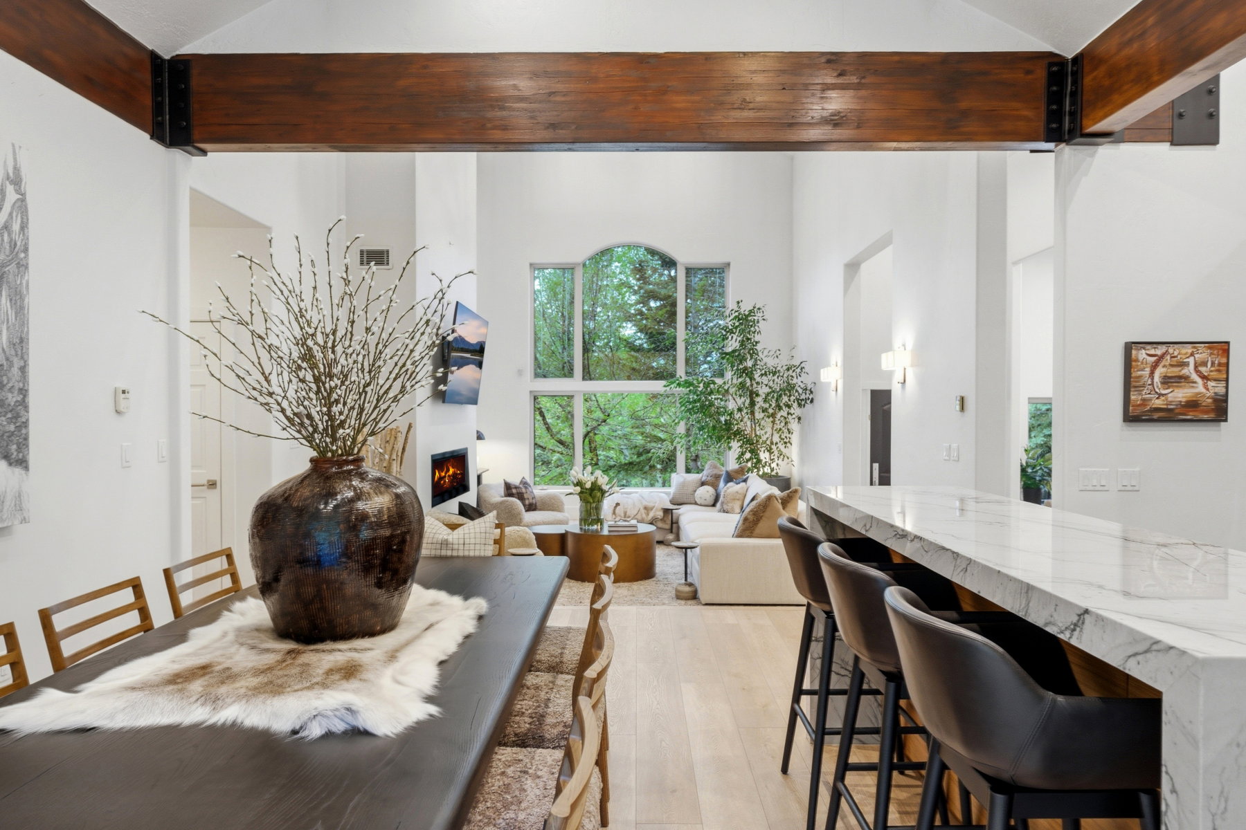 Open-concept living space featuring high vaulted ceilings with exposed wood beams, a prominent fireplace, and expansive windows