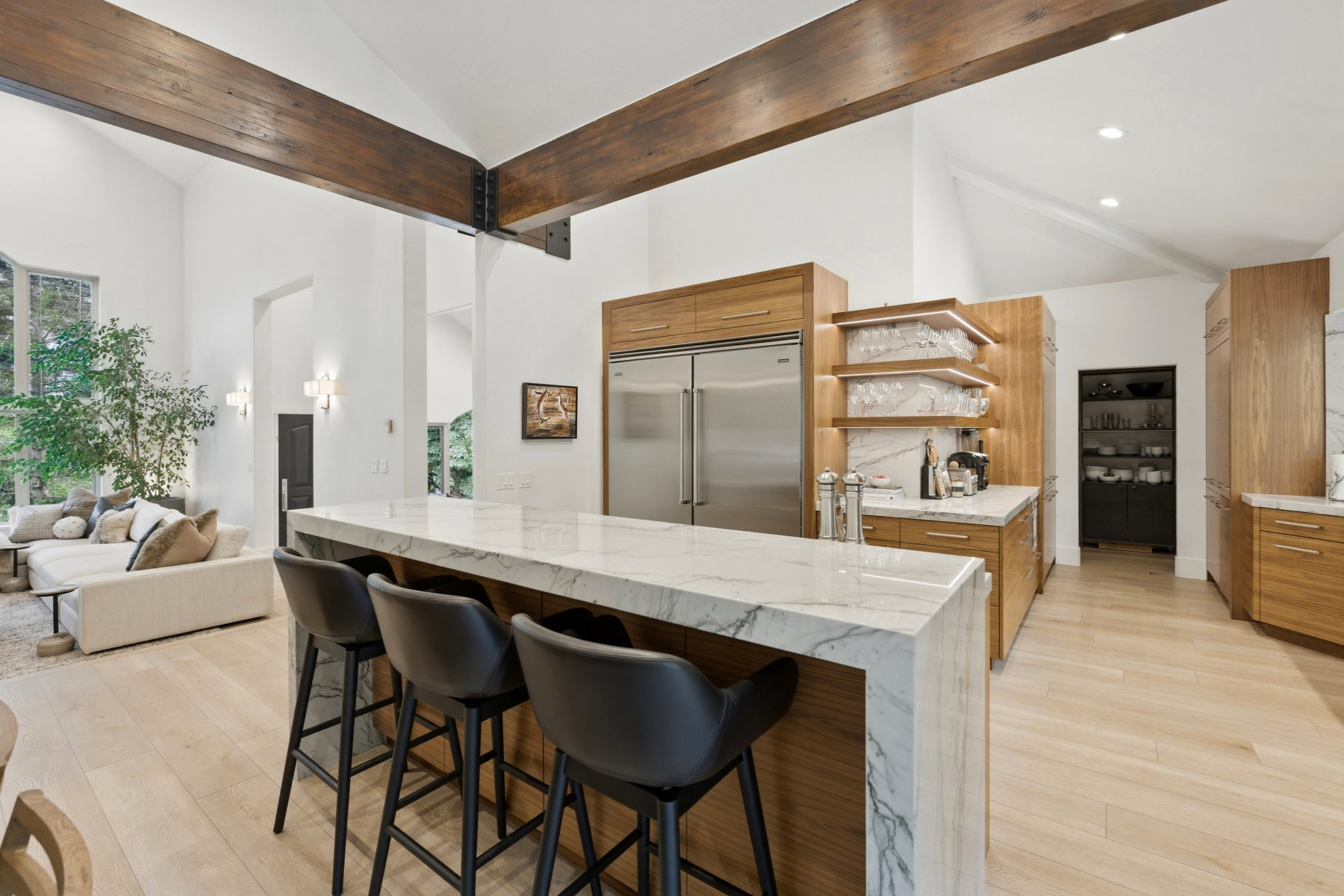 Kitchen featuring a marble waterfall island with seating, stainless steel appliances, light wood-finish cabinetry, and recessed lighting