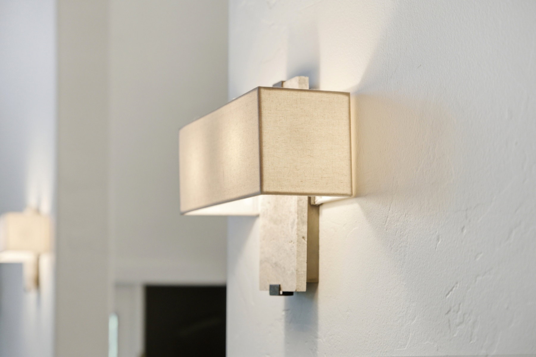 Wall-mounted sconce lighting with a rectangular fabric shade and stone-look backing, providing accent illumination