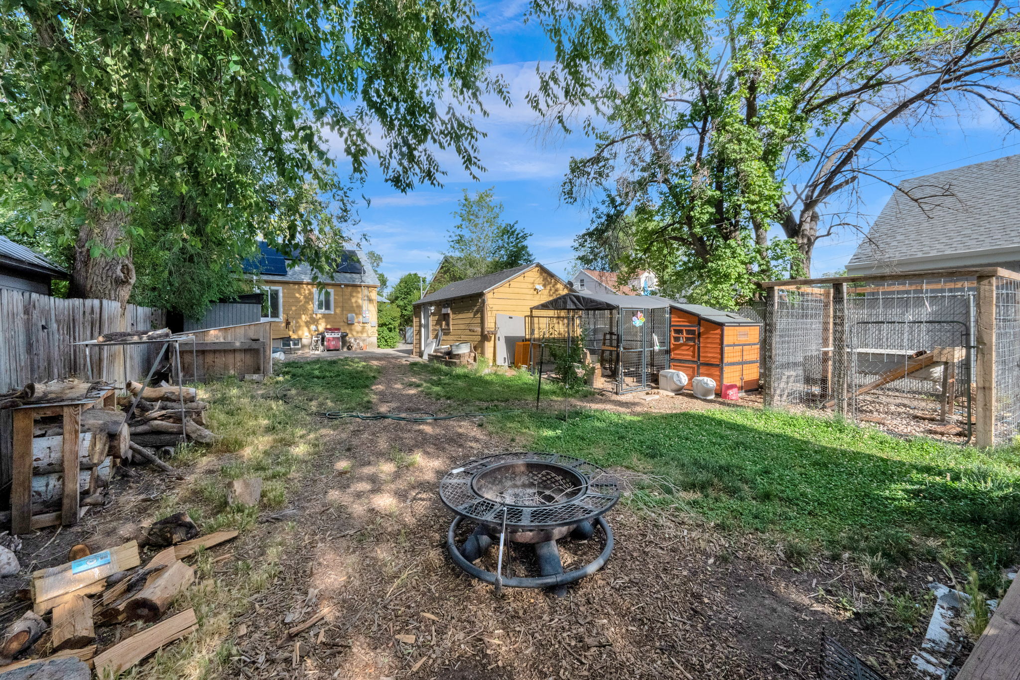 Expansive backyard with a central fire pit, established trees, and multiple outbuildings