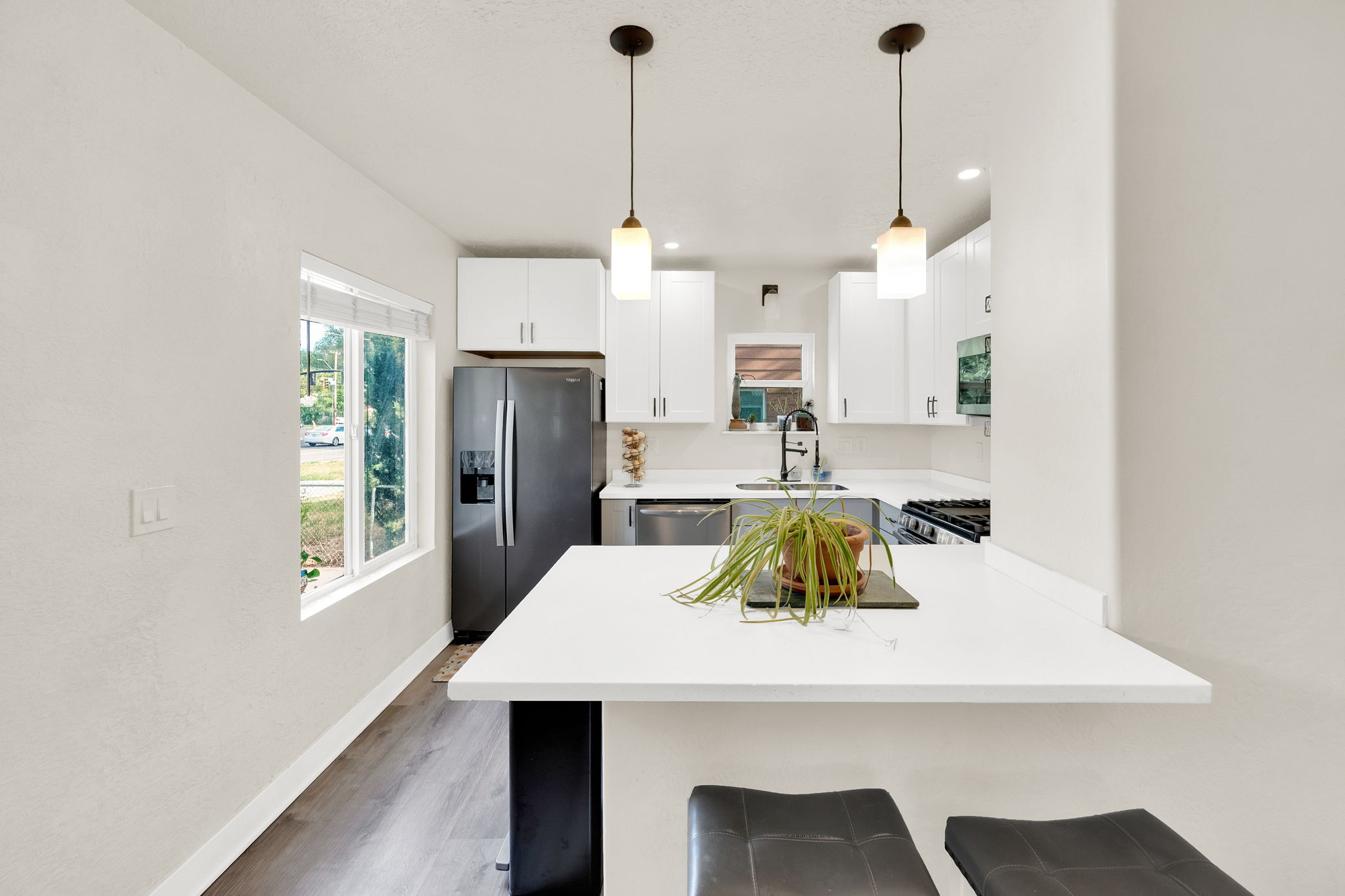 Kitchen featuring white shaker cabinetry, stainless steel appliances, quartz countertops, a kitchen island with seating, and wood-finish flooring