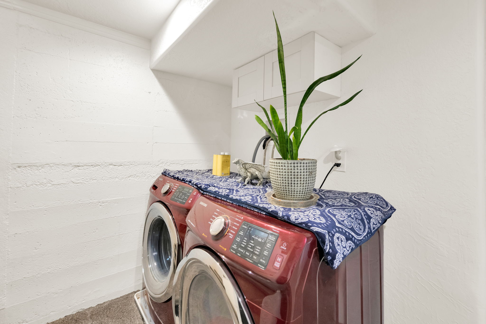 Dedicated laundry area featuring a front-load washer and dryer set, white overhead cabinetry, and textured white walls