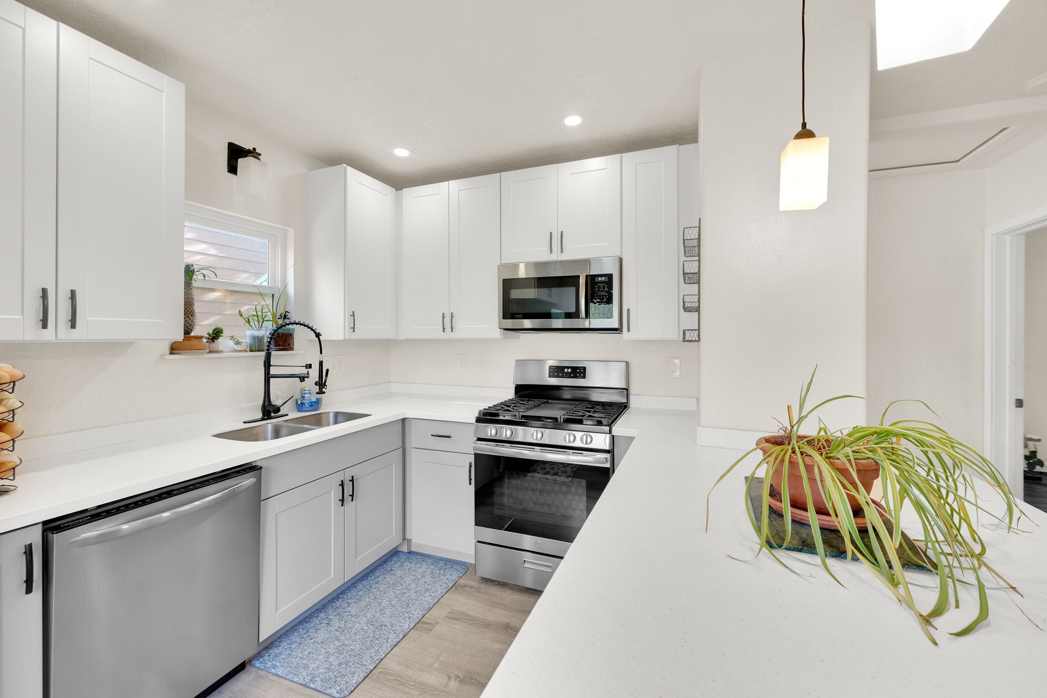 Kitchen featuring white upper cabinetry, gray lower cabinetry, stainless steel appliances, a double basin sink with a matte black faucet, and light wood-finish flooring