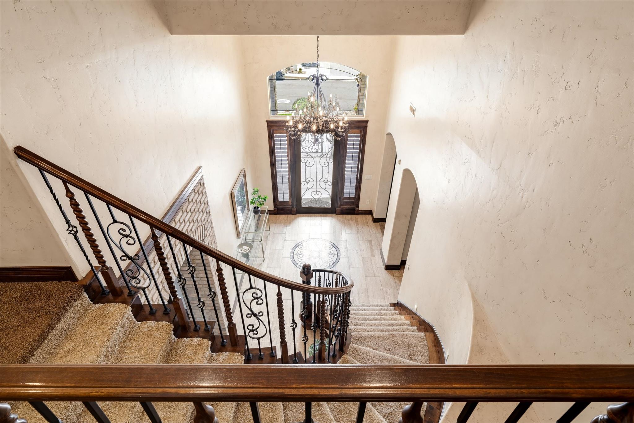 Grand entryway featuring a decorative chandelier, arched doorways, and a wood-finish double entry door with wrought iron detailing