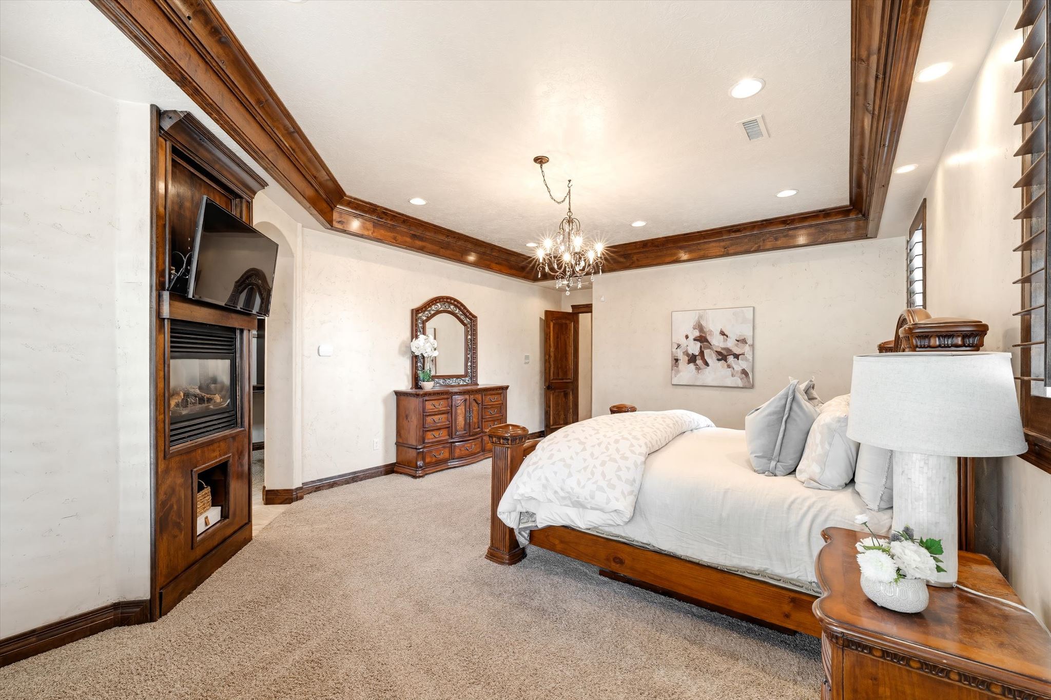 Spacious room featuring a tray ceiling with wood beam accents, recessed lighting, and a central chandelier