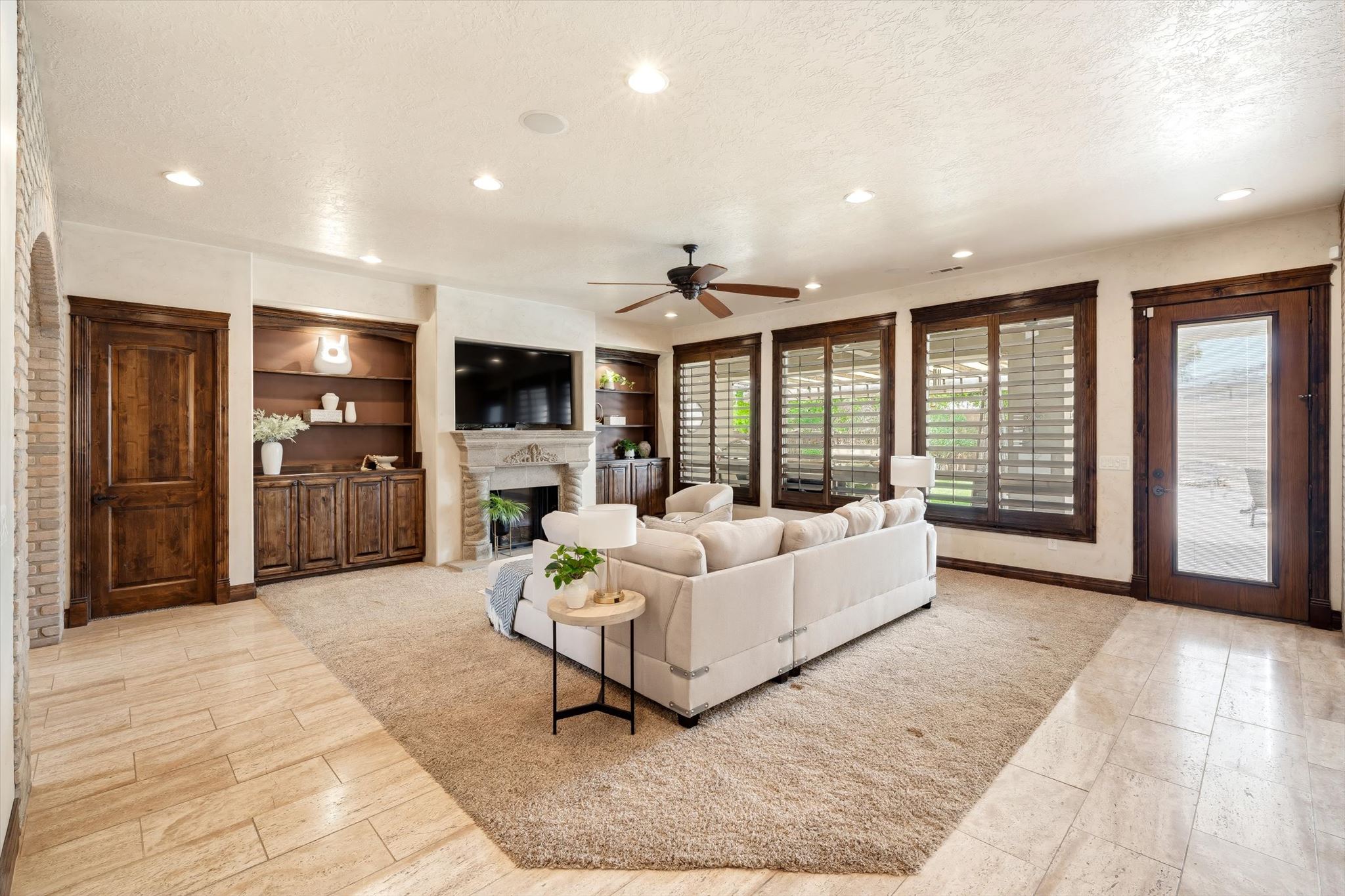 Spacious living area featuring a stone fireplace, built-in cabinetry, recessed lighting, wood-finish doors, and plantation shutters