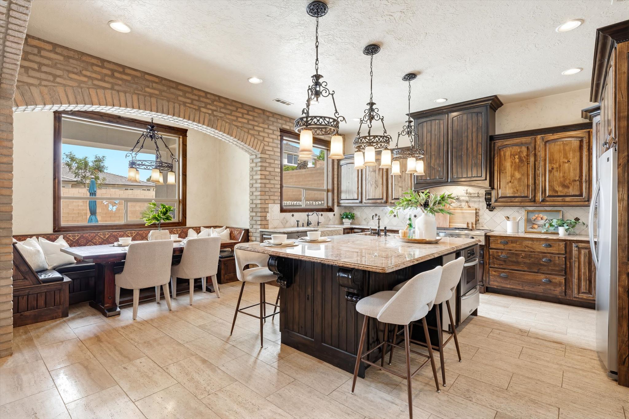 Open-concept kitchen featuring an oversized island with countertop seating, wood cabinetry, stone countertops, and tile flooring