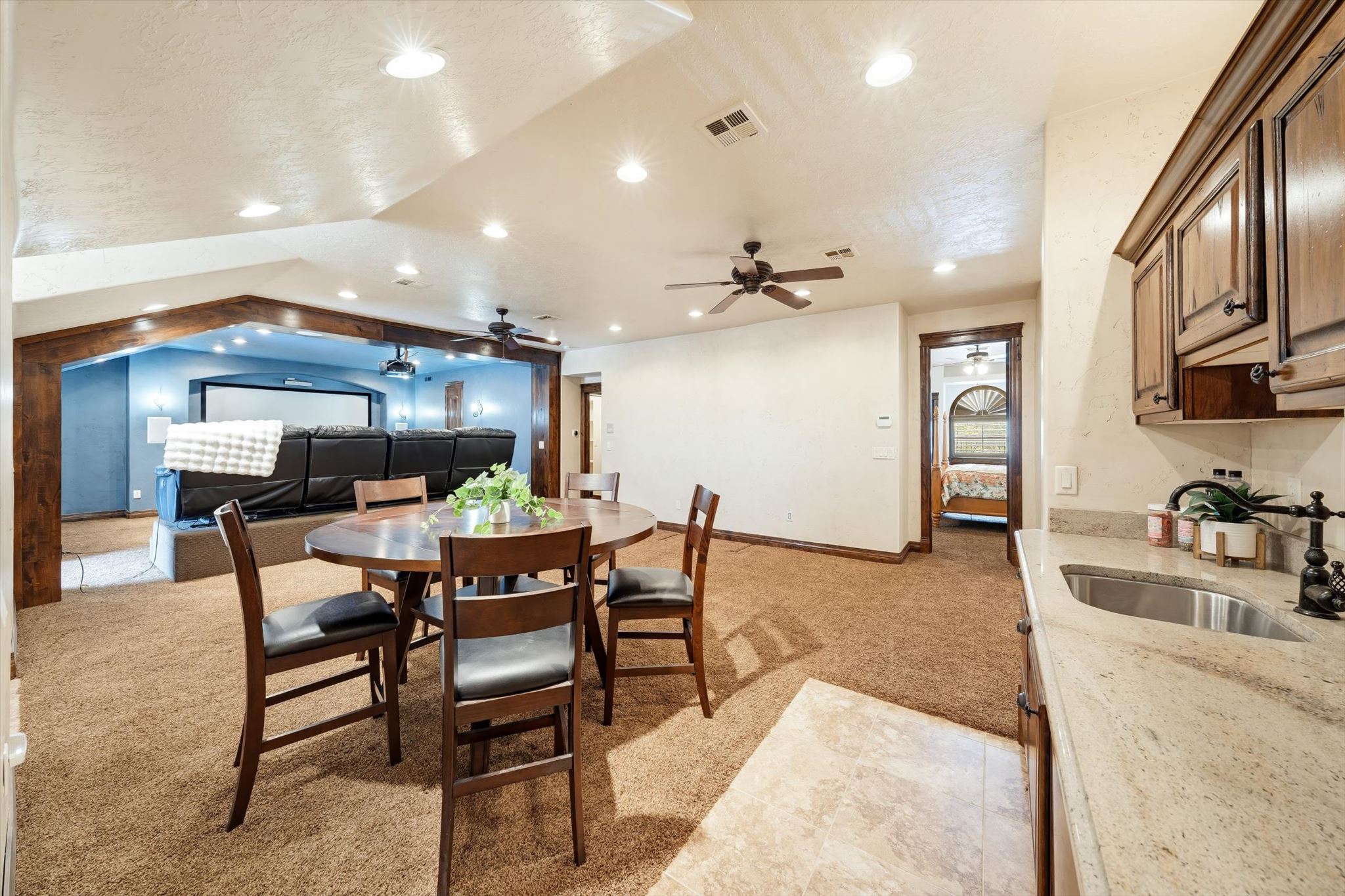 Entertainment area featuring a defined media room with a projector and screen, recessed lighting, a ceiling fan, a built-in wet bar with a stainless steel sink, and light-toned countertops