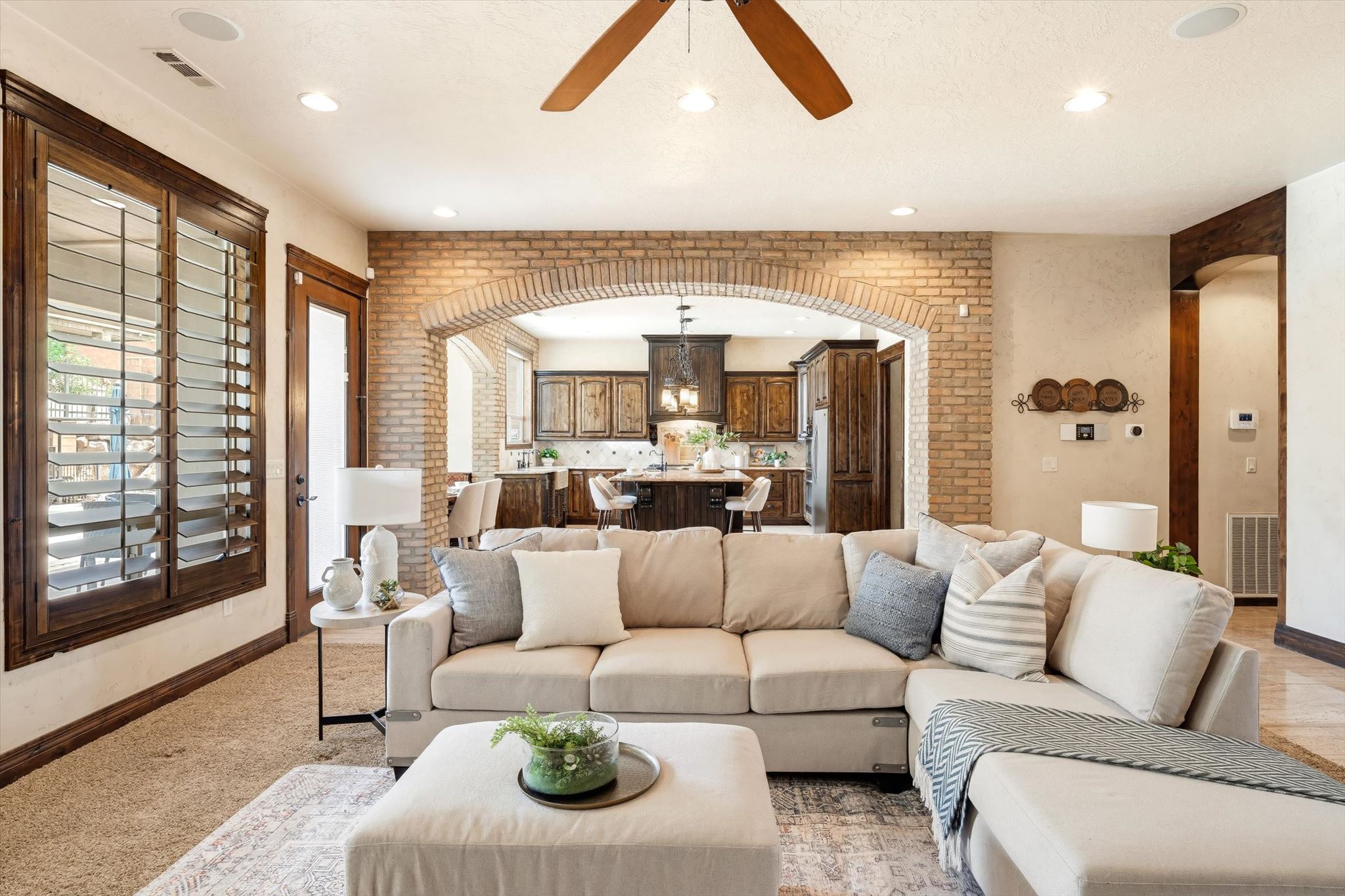 Open-concept living space featuring a brick arched doorway, wood-finish window shutters, recessed lighting, a ceiling fan, and carpeted flooring