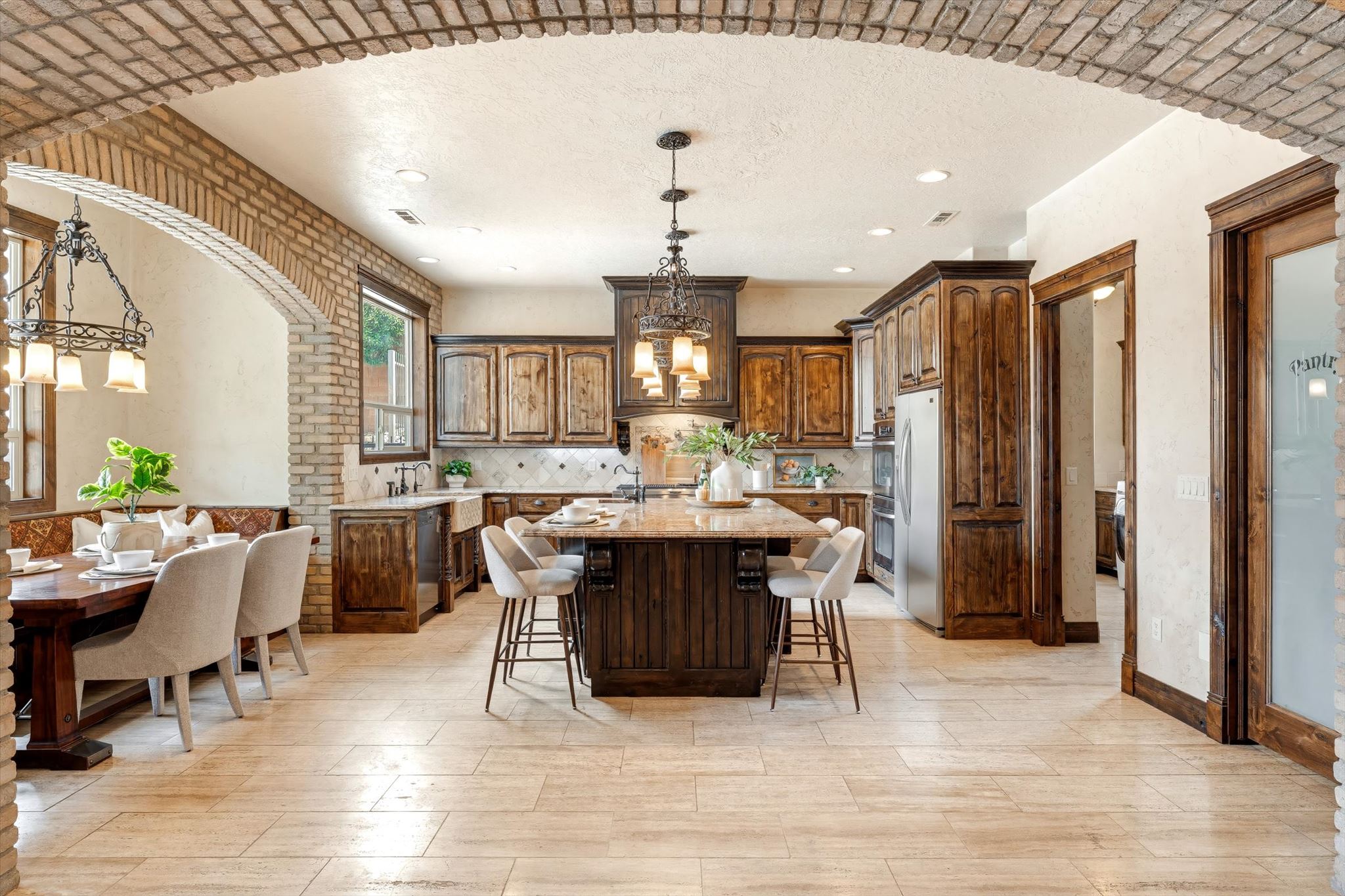 Kitchen and dining area featuring a brick archway, wood-finish flooring, custom wood cabinetry, a large kitchen island with seating, and a farmhouse sink