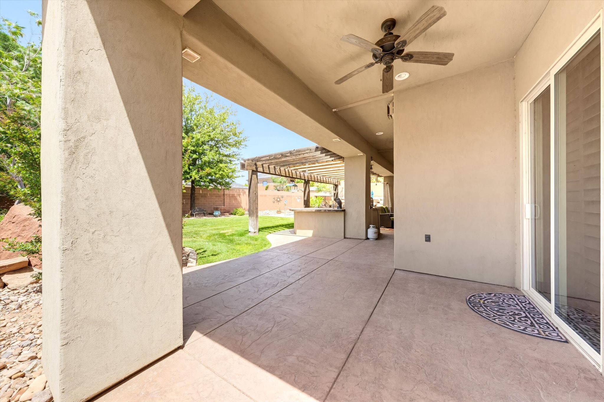 Covered patio with stamped concrete flooring, ceiling fan, and sliding glass door