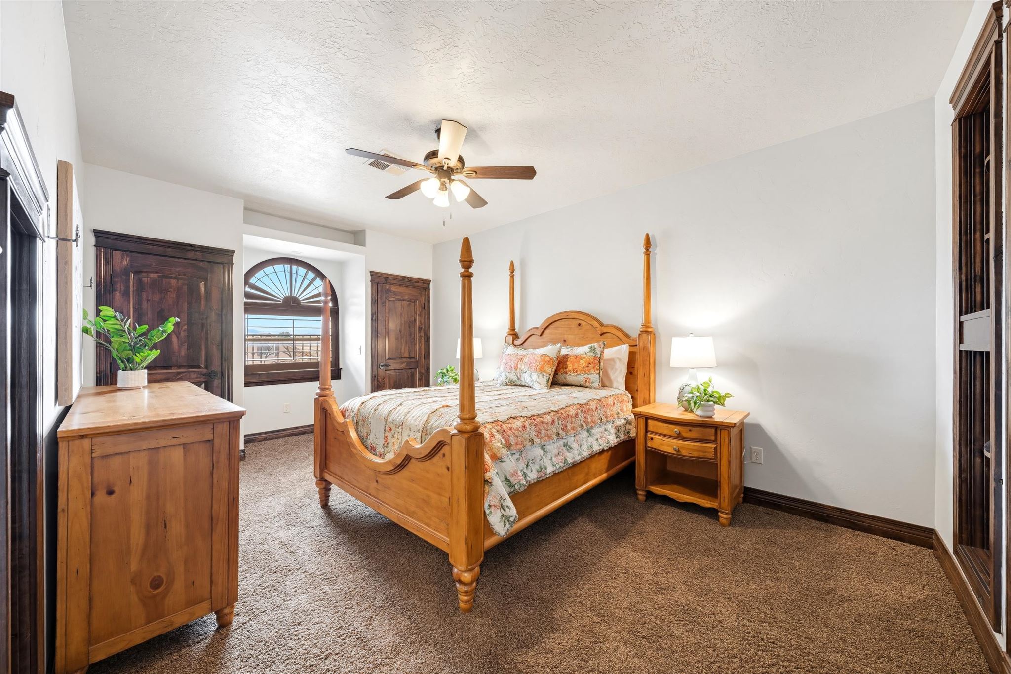 Bedroom featuring a prominent arched window with sunburst blinds, brown carpet, and a ceiling fan
