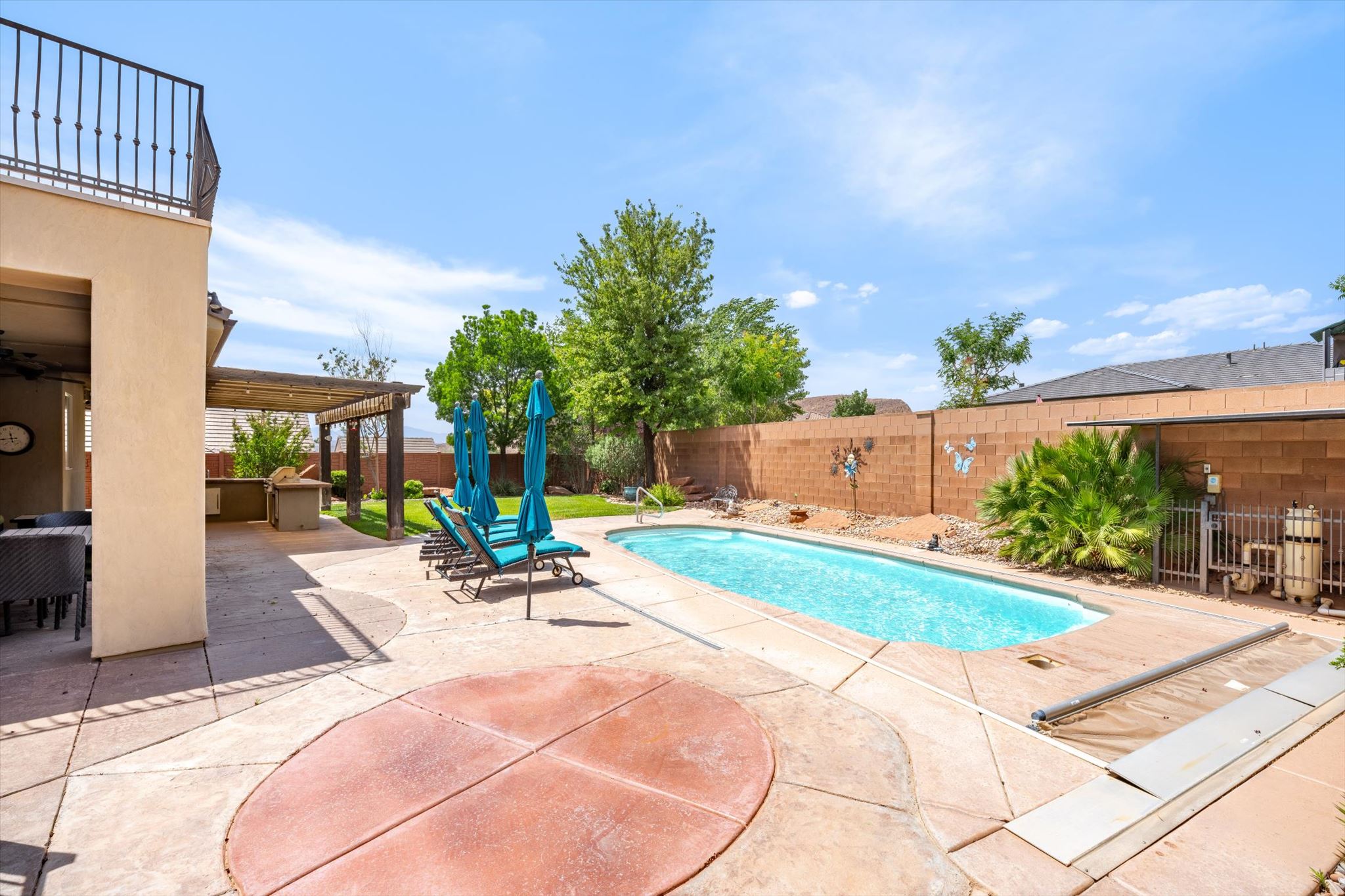 Outdoor oasis featuring a rectangular swimming pool, spacious concrete patio, pergola-covered outdoor kitchen, and second-story balcony