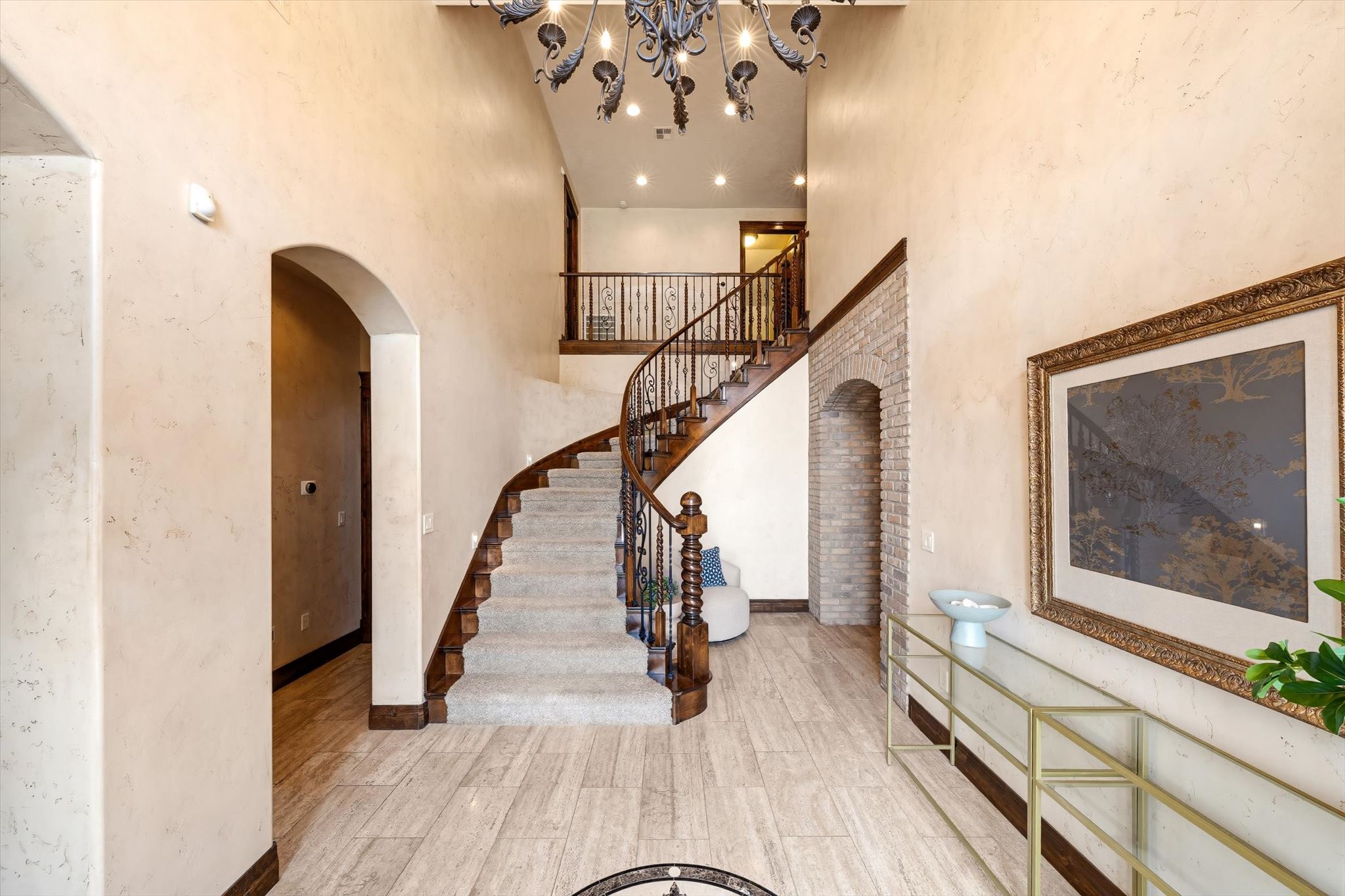 Foyer featuring a grand curved staircase with ornate wrought iron railings, high ceilings, arched doorways, and light-toned tile flooring