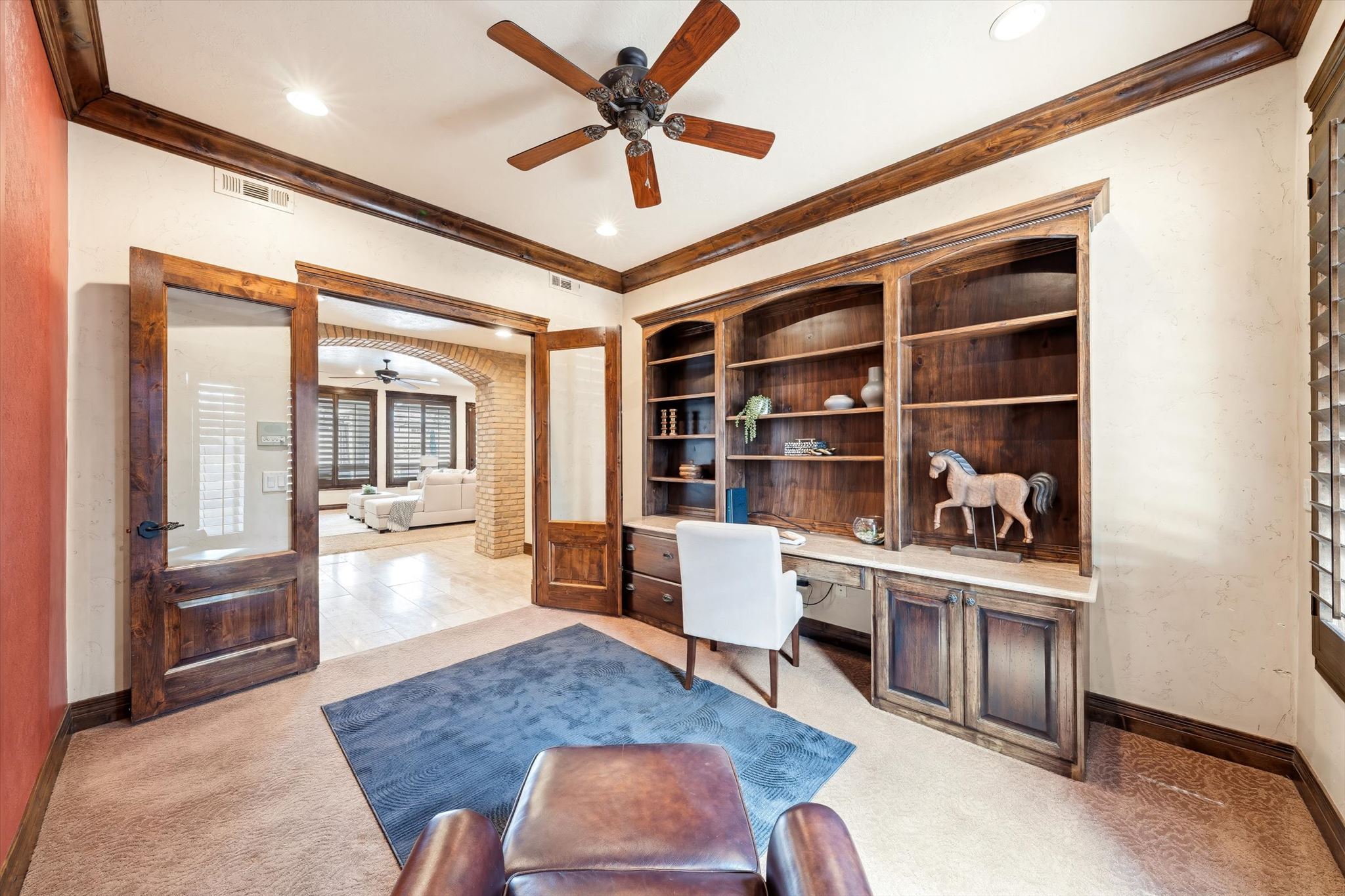 Office space featuring rich wood-finish built-in shelving, a coordinating desk, and glass-paneled double doors