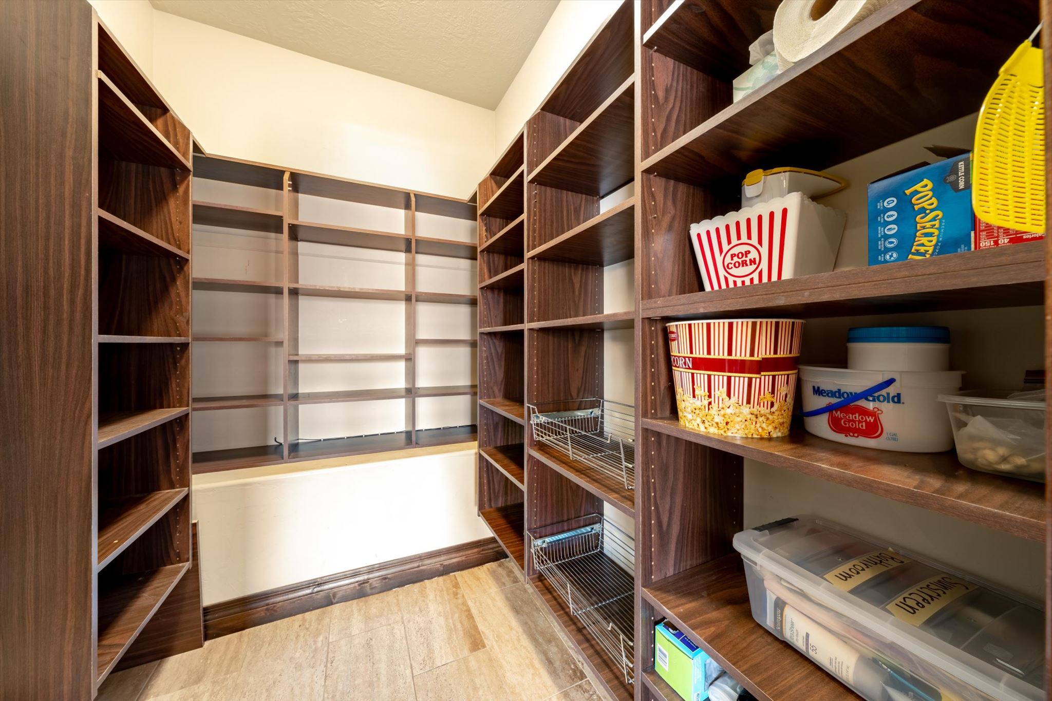 Spacious pantry featuring extensive wood-finish shelving, integrated pull-out wire baskets, and light-toned flooring