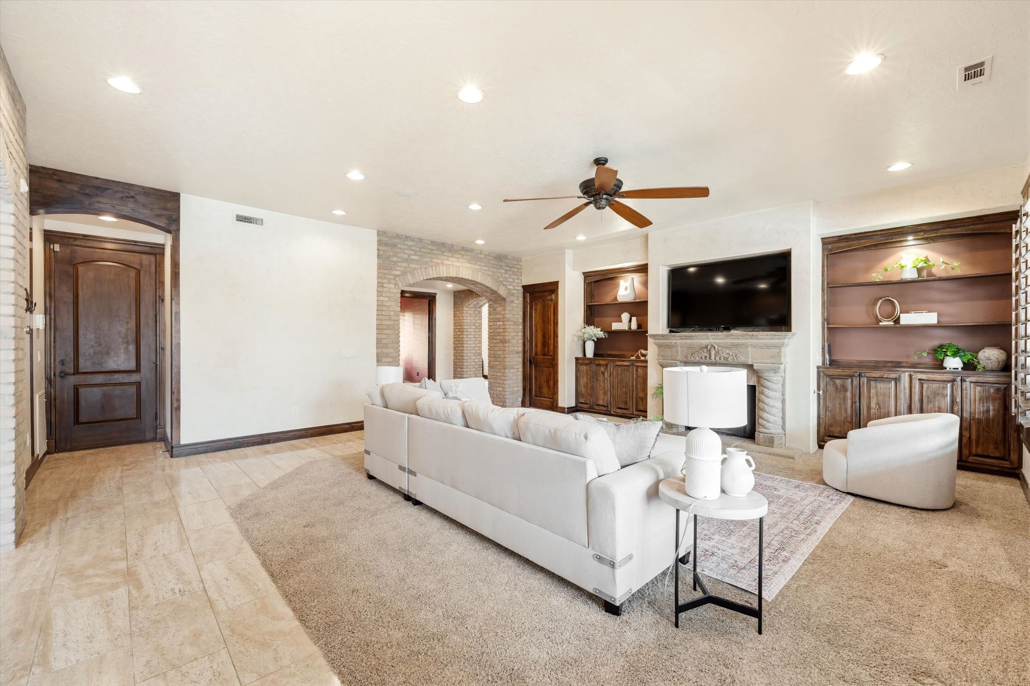 Spacious living area featuring a central fireplace with an ornate mantel, built-in shelving, recessed lighting, and a ceiling fan