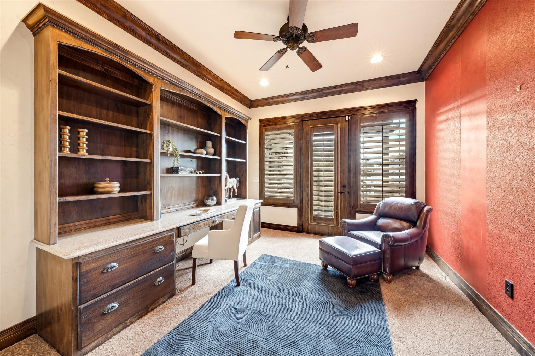 Built-in wood cabinetry with integrated desk and shelving, stone countertop, wood-framed double doors with plantation shutters, ceiling fan, and recessed lighting