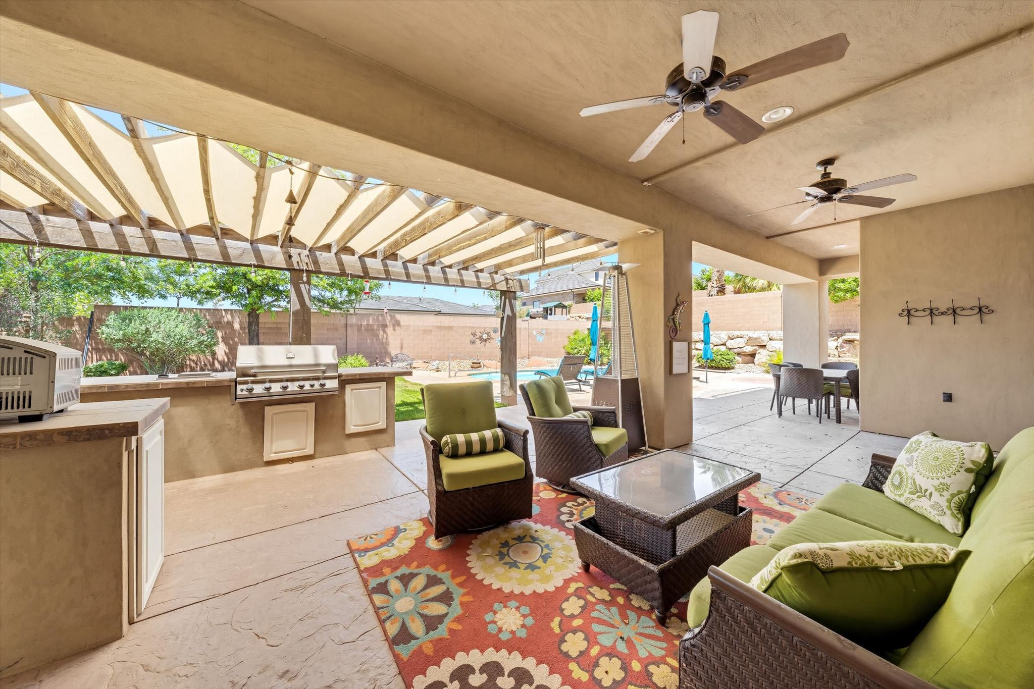 Covered patio featuring stamped concrete flooring, a built-in outdoor kitchen with grill, ceiling fans, and a pergola with shading
