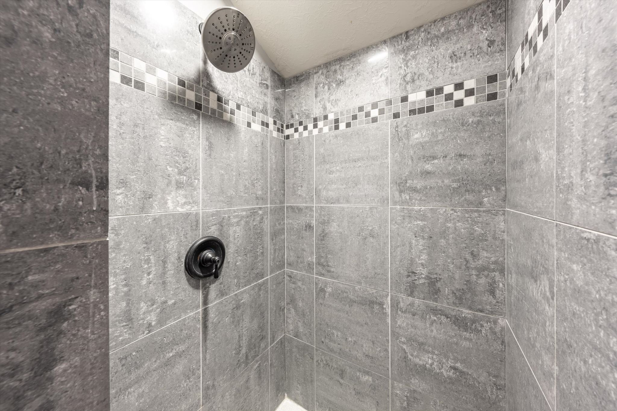 Shower enclosure featuring gray stone-look wall tiles with a decorative mosaic accent band