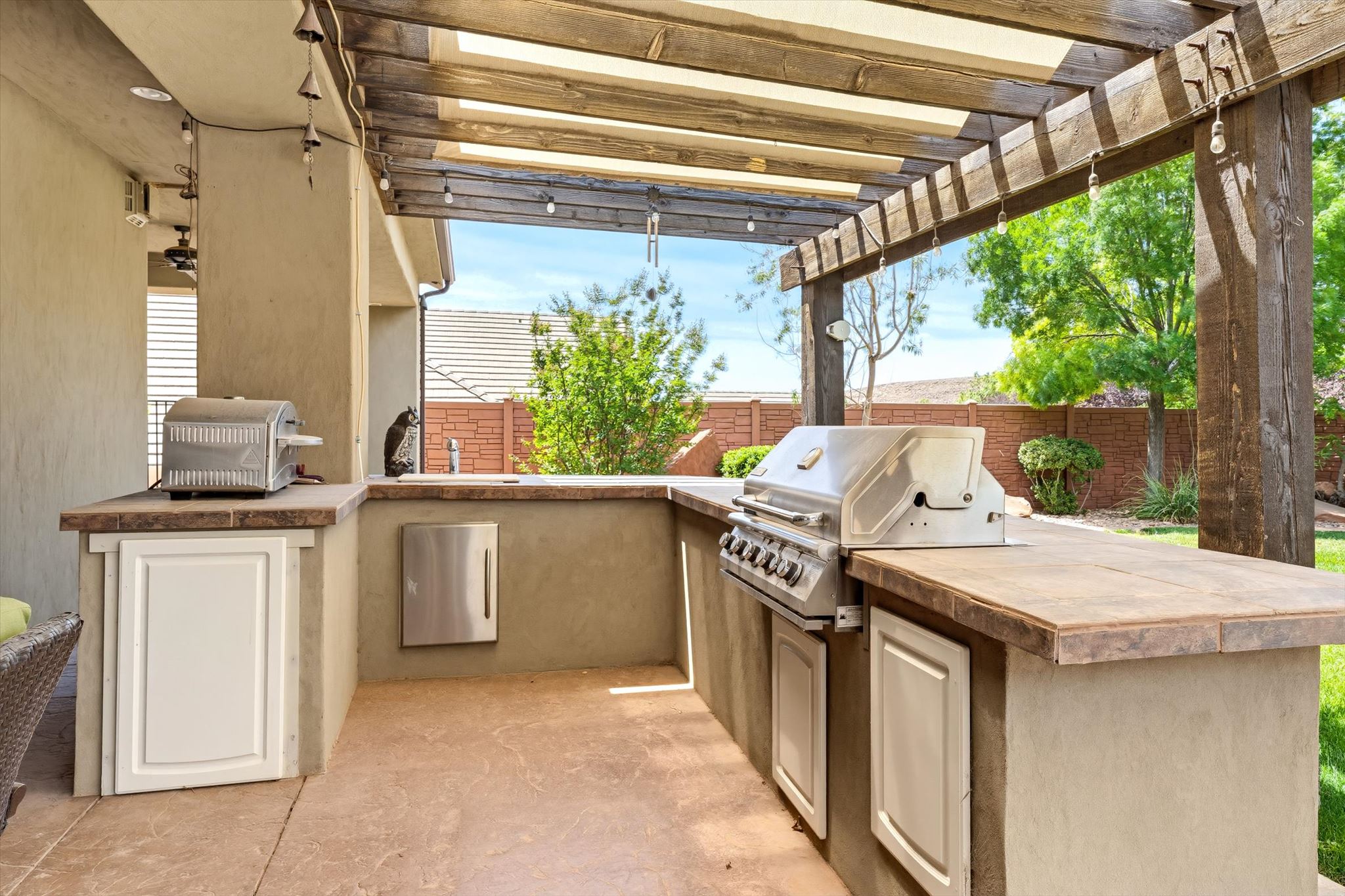 Outdoor kitchen featuring a built-in stainless steel grill, integrated storage cabinetry, and a tile countertop