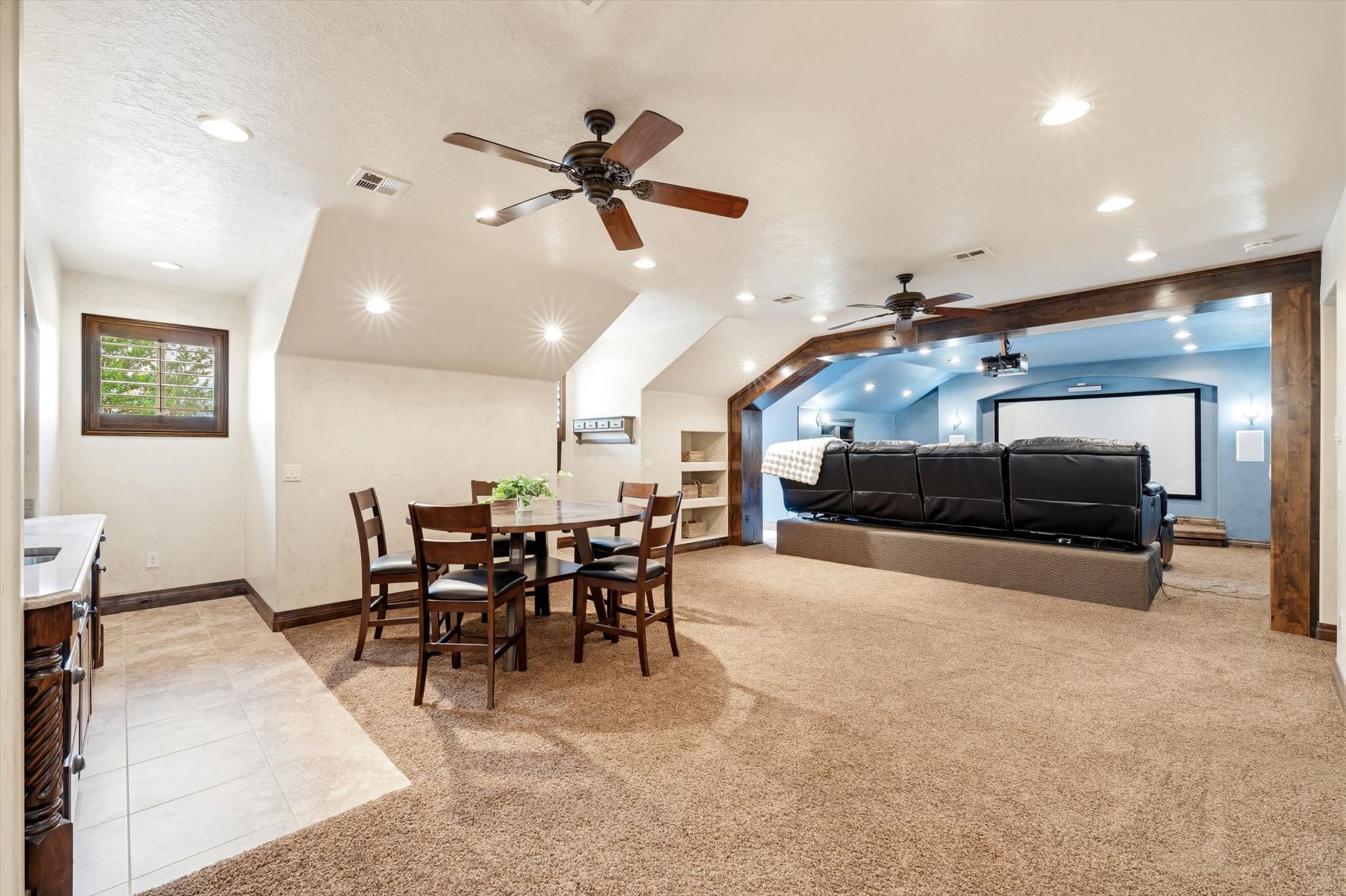 Spacious entertainment area featuring recessed lighting, a built-in media screen, exposed wood beams, and a dining area with tile flooring and a built-in countertop