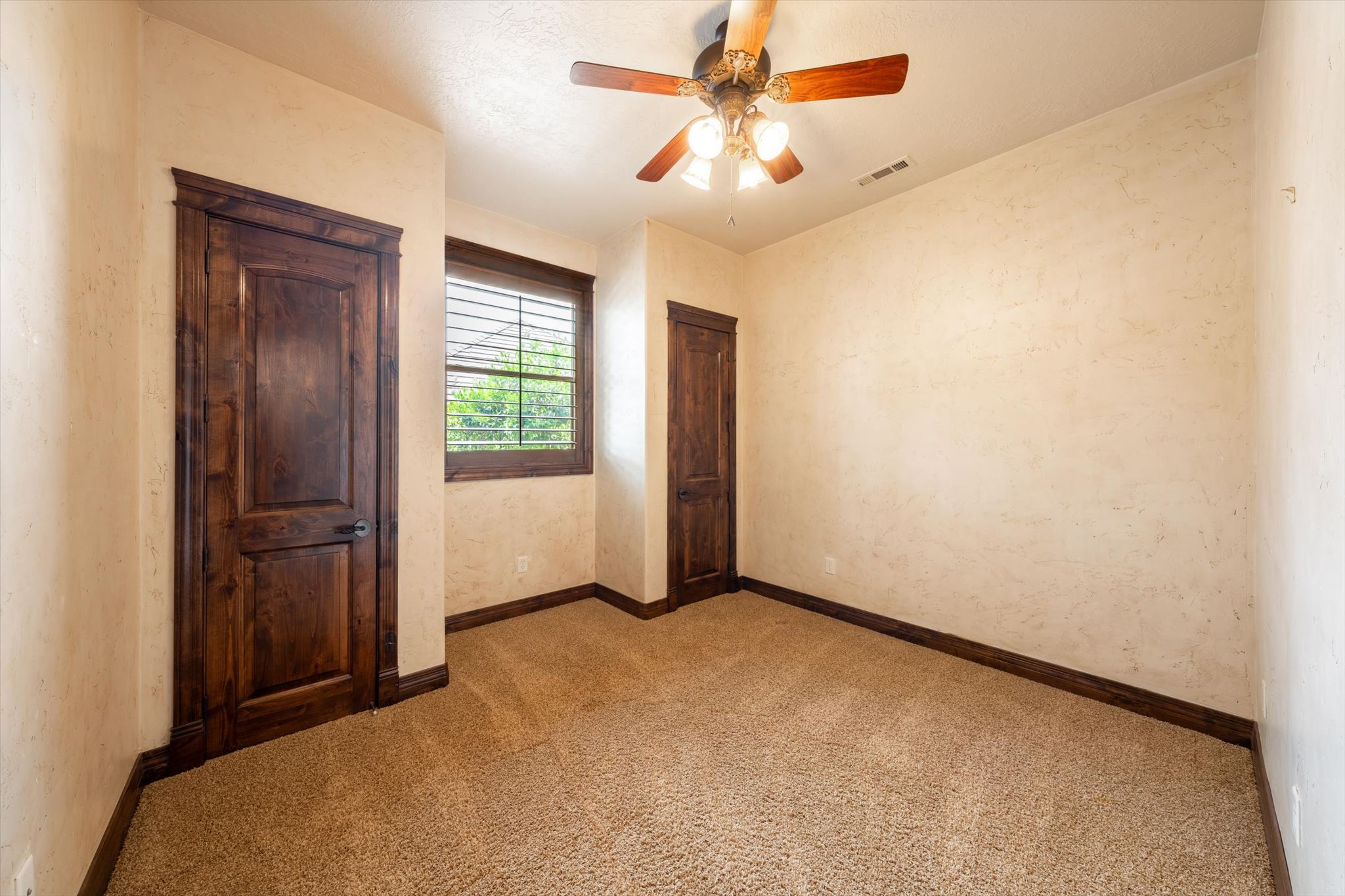 Carpeted room featuring textured walls, a ceiling fan with light fixture, and a window with wood-finish blinds