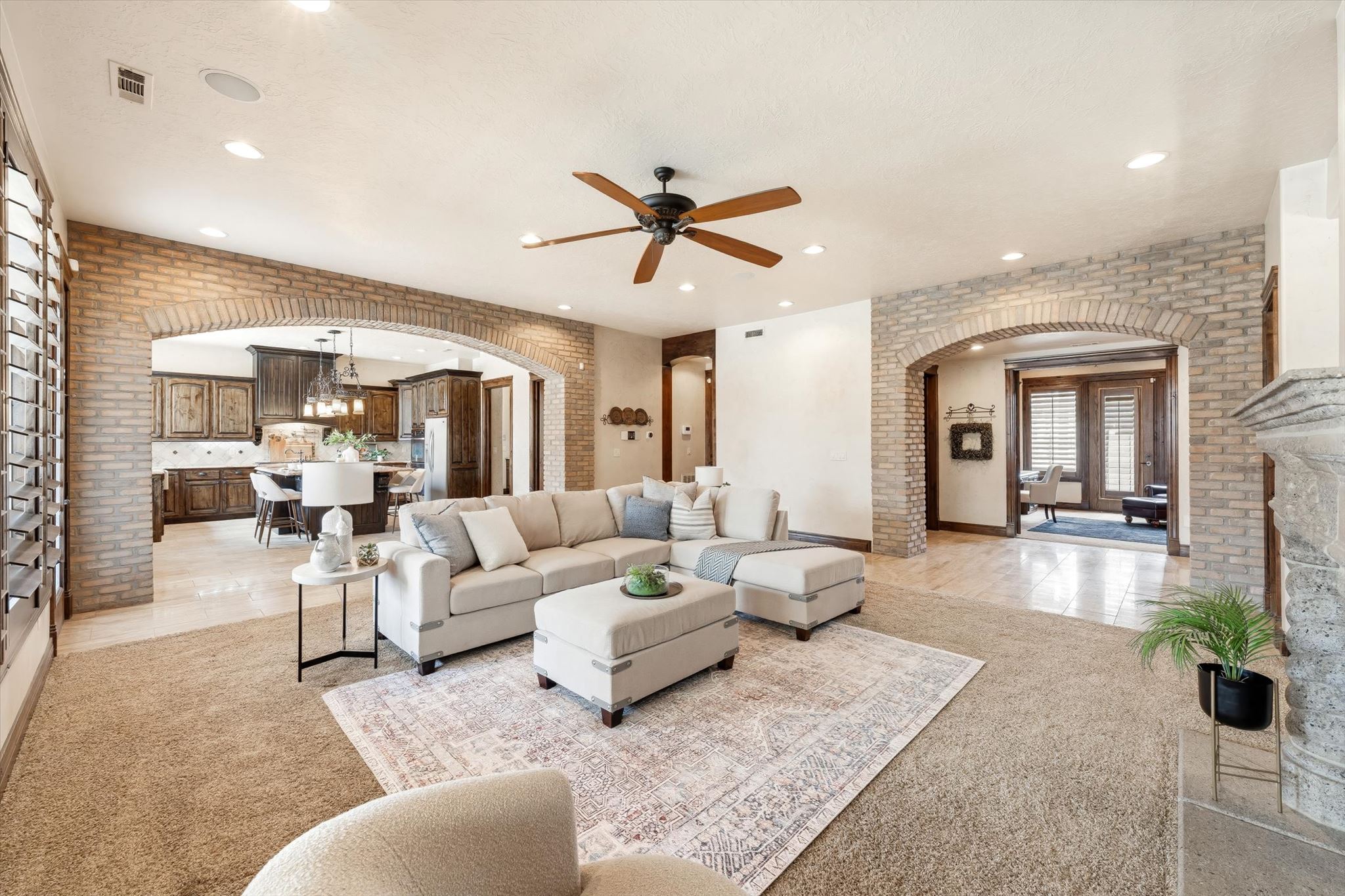 Spacious living area featuring exposed brick archways, recessed lighting, and a ceiling fan