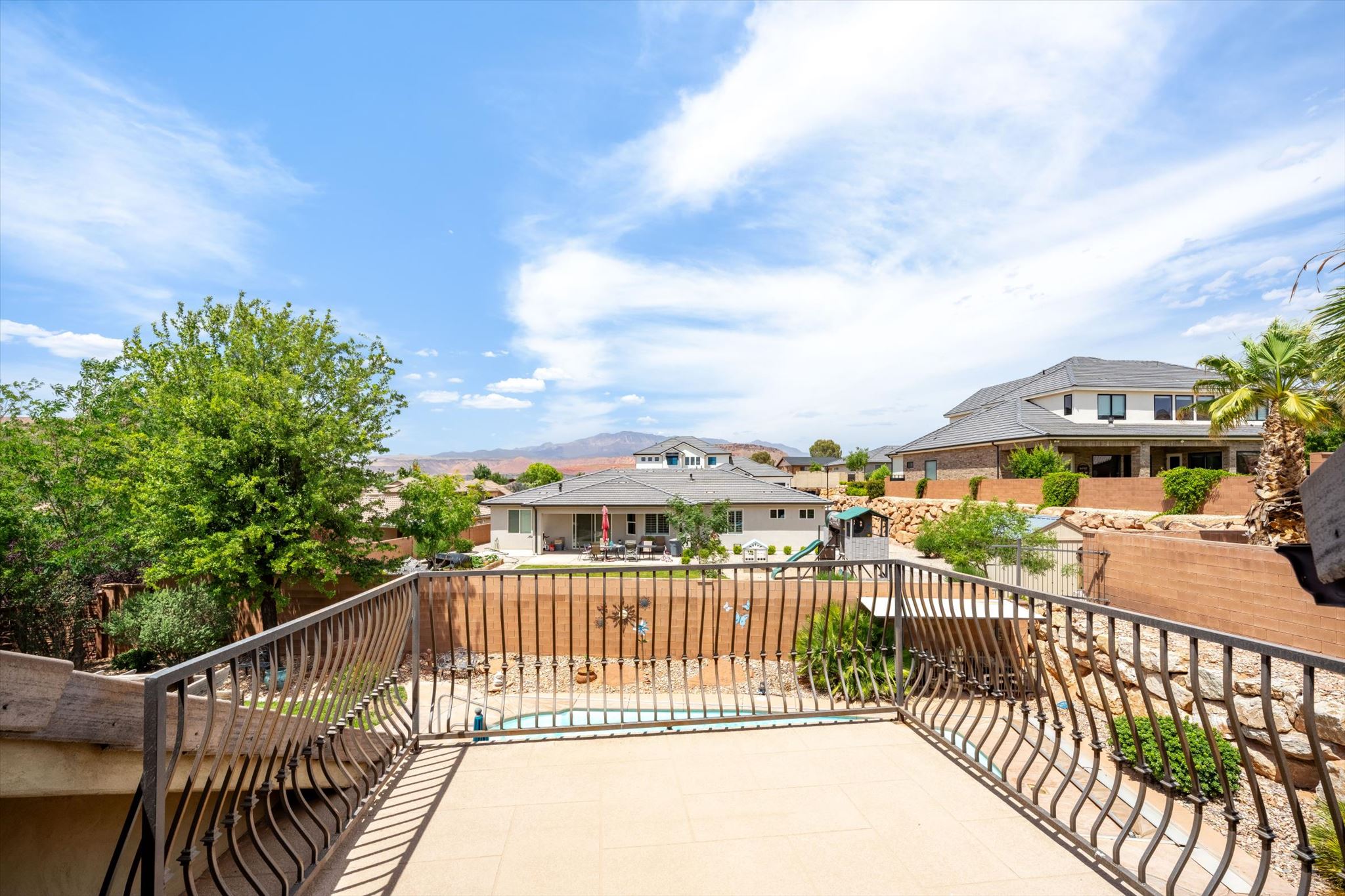 Outdoor balcony with wrought iron railing, light-colored tile flooring, and distant mountain scenery