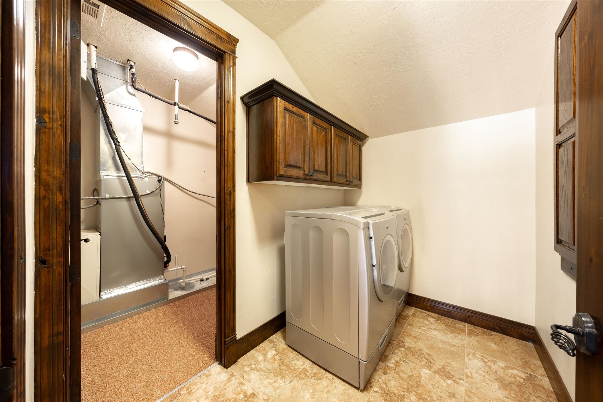 Laundry room featuring tile flooring, dark wood cabinetry, and a utility closet with a mechanical system