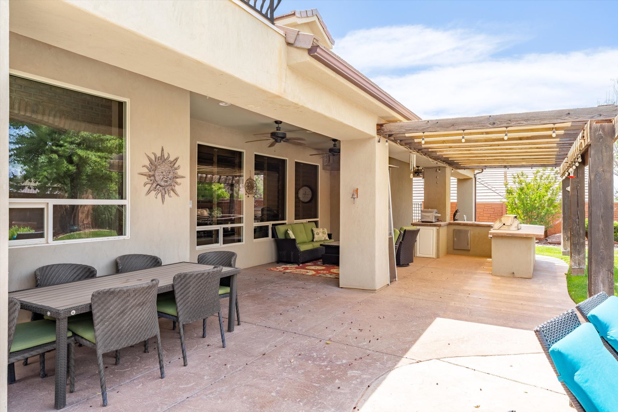 Expansive outdoor patio featuring an integrated outdoor kitchen, a wood pergola with string lighting, and a covered section with ceiling fans