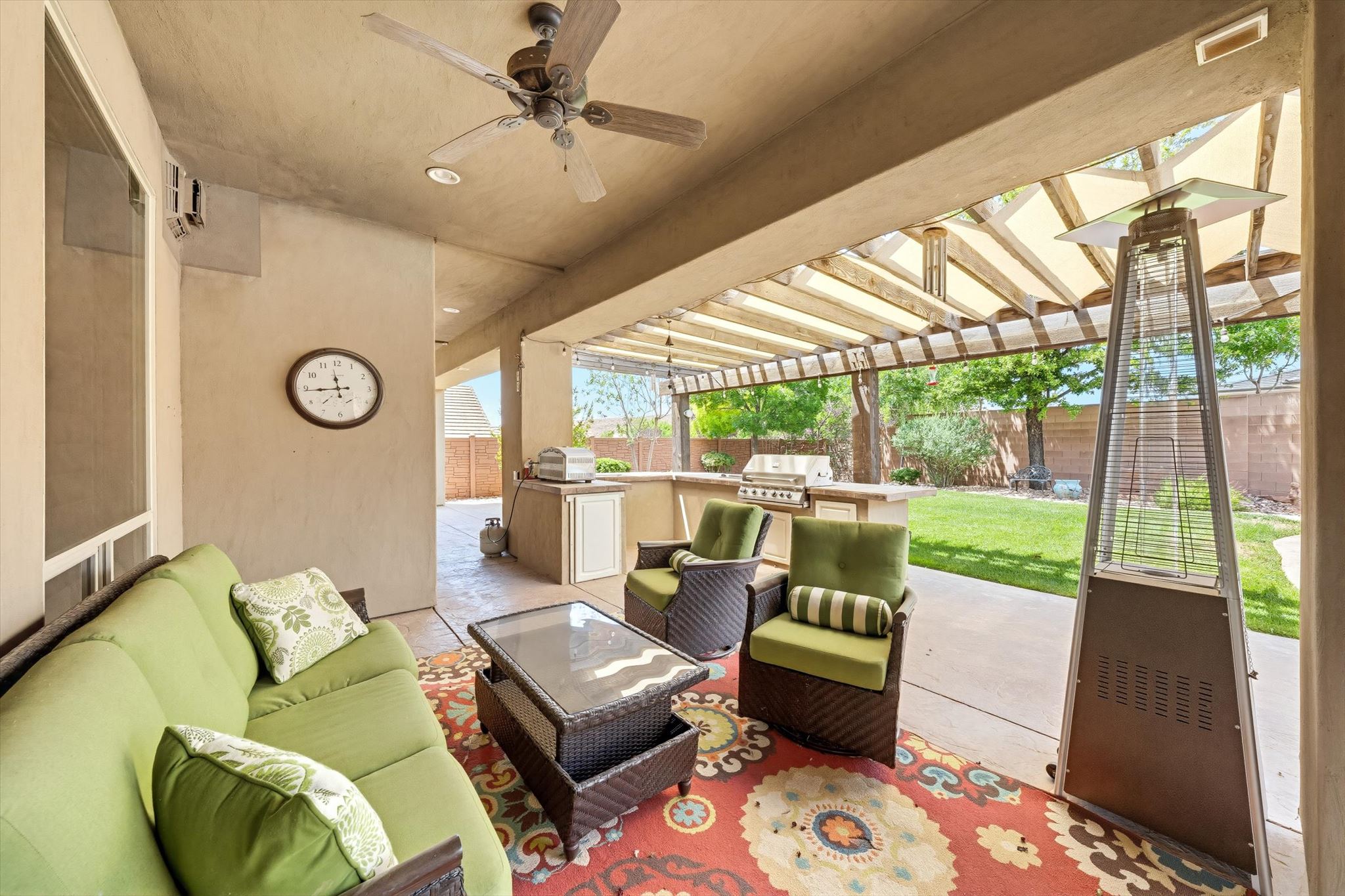 Covered patio featuring an outdoor kitchen with built-in grill, open pergola extension, and a ceiling fan