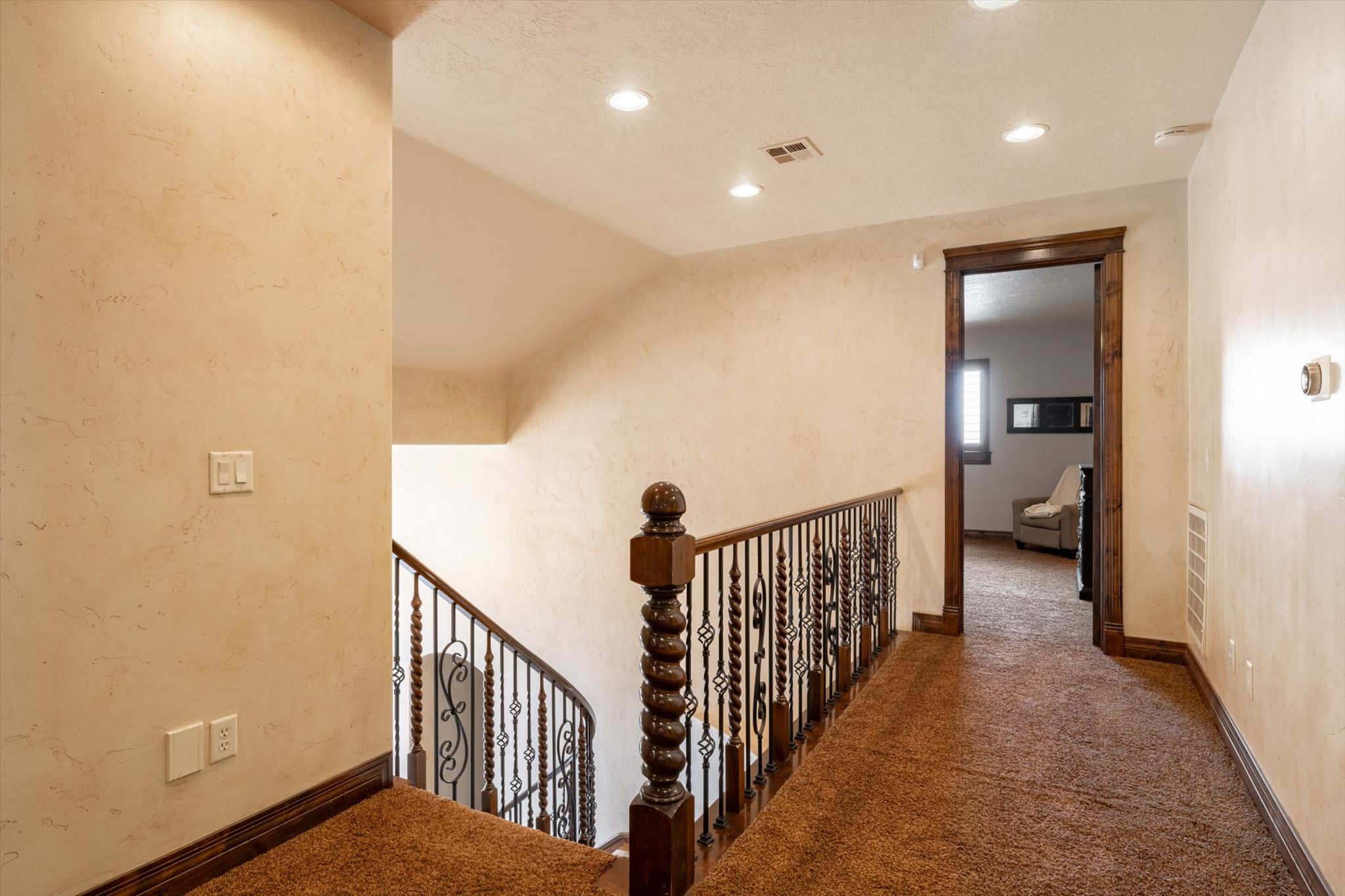 Staircase featuring wrought iron balusters with ornate scrollwork, a dark wood newel post, and matching handrail