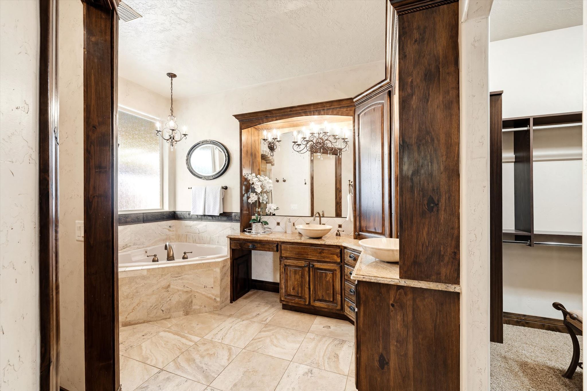 Spacious bathroom featuring a corner soaking tub with stone surround, dual vanity with vessel sinks, and ample wood cabinetry