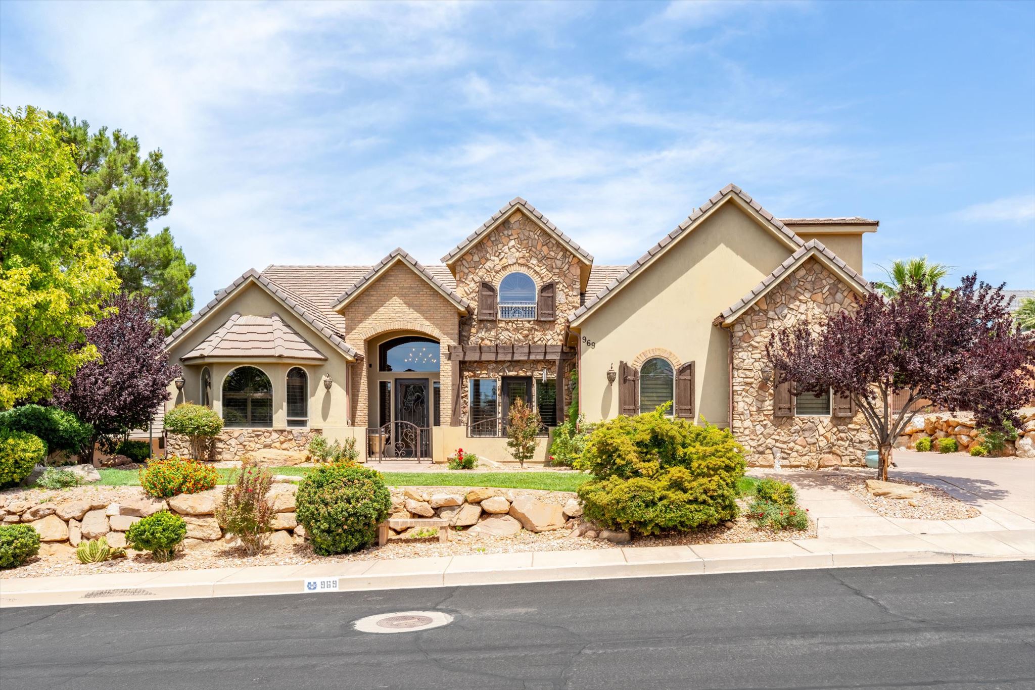 Stucco and stone exterior featuring multiple gabled rooflines, arched windows, decorative shutters, and a prominent arched entryway