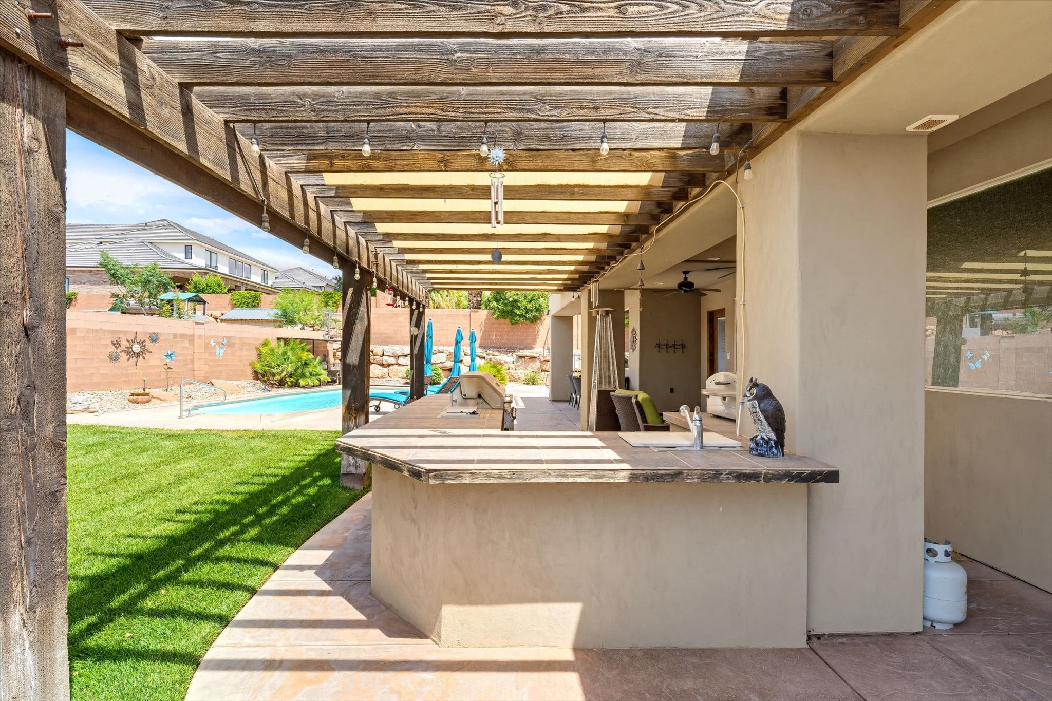 Covered patio with exposed wood pergola featuring an outdoor kitchen with integrated grill and sink