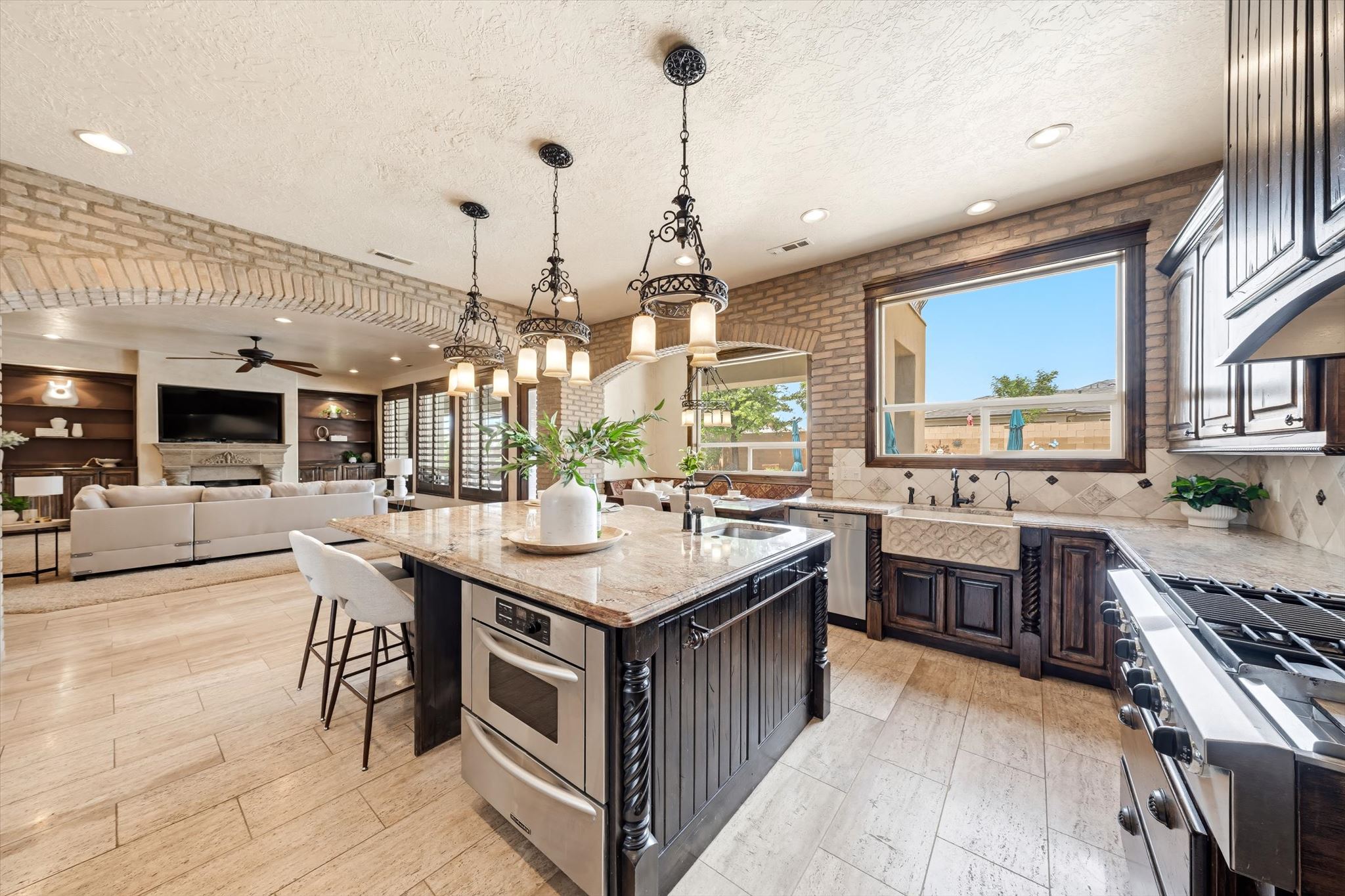 Spacious kitchen featuring a large central island with integrated microwave, granite countertops, tile backsplash, and a farmhouse sink