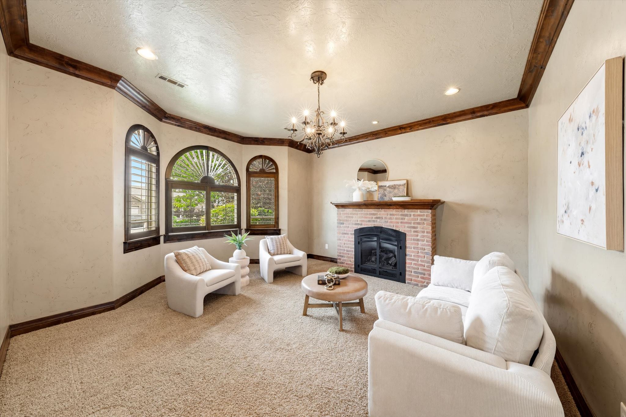 Living area featuring a brick fireplace with a wood-mantel, arched windows, and crown molding