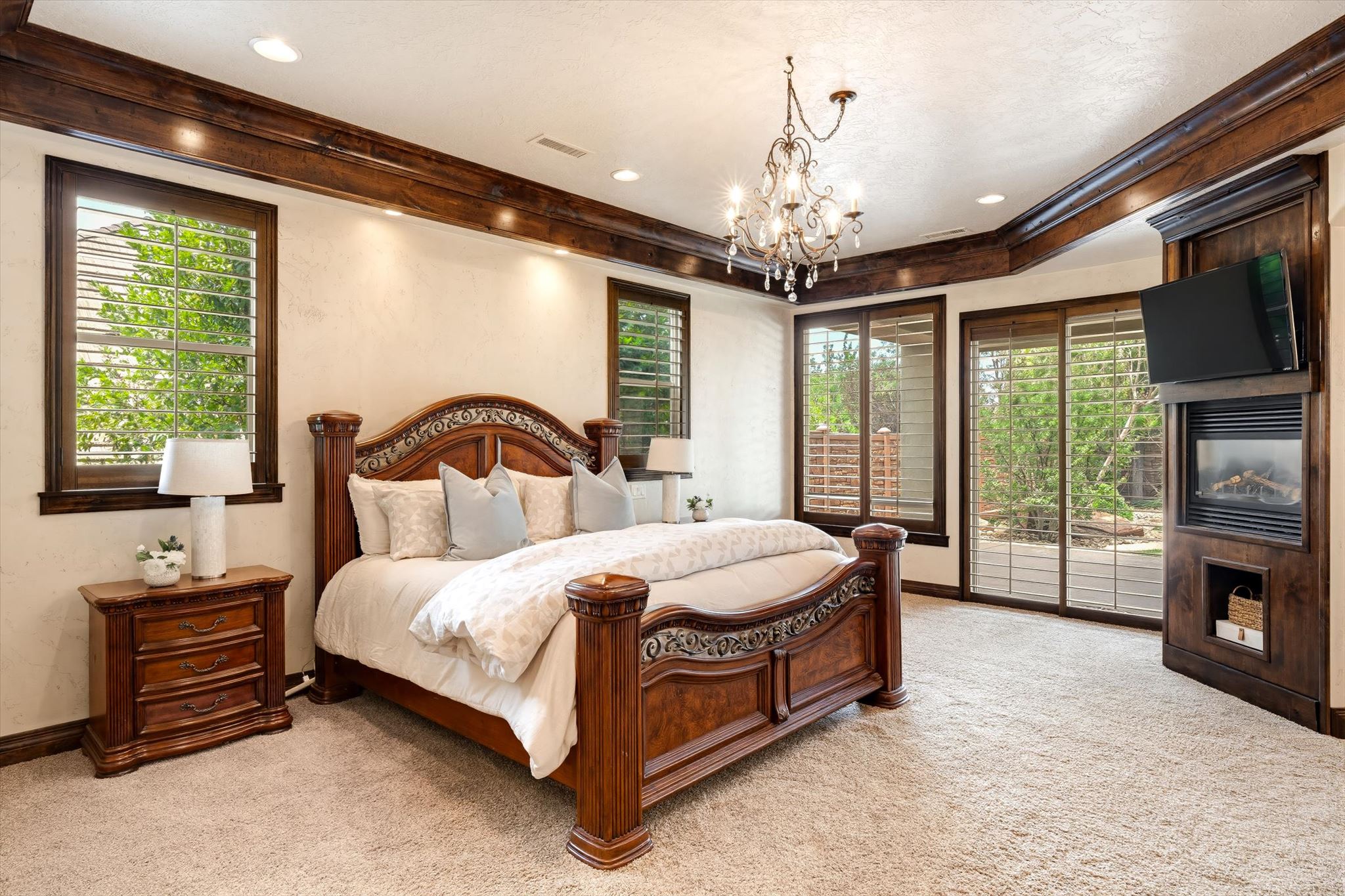 Carpeted room featuring a built-in fireplace, wood-framed windows with louvered shutters, exposed wood ceiling beams, and a chandelier