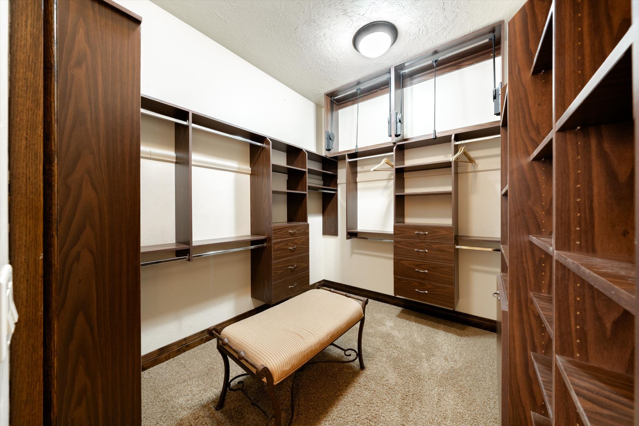 Walk-in closet featuring extensive dark wood-finish built-in shelving, hanging rods, and multiple drawer units