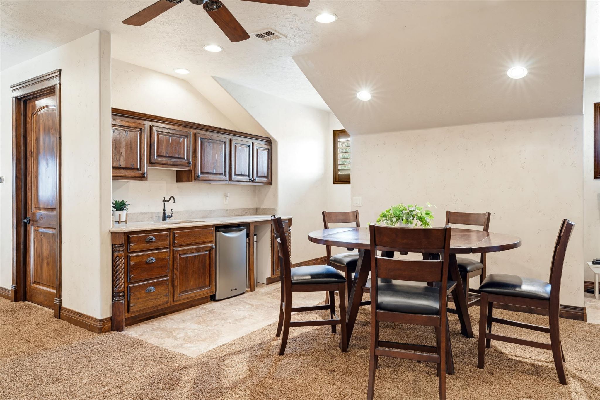 Integrated wet bar featuring wood cabinetry, stone countertop, undermount sink with gooseneck faucet, and a built-in beverage refrigerator