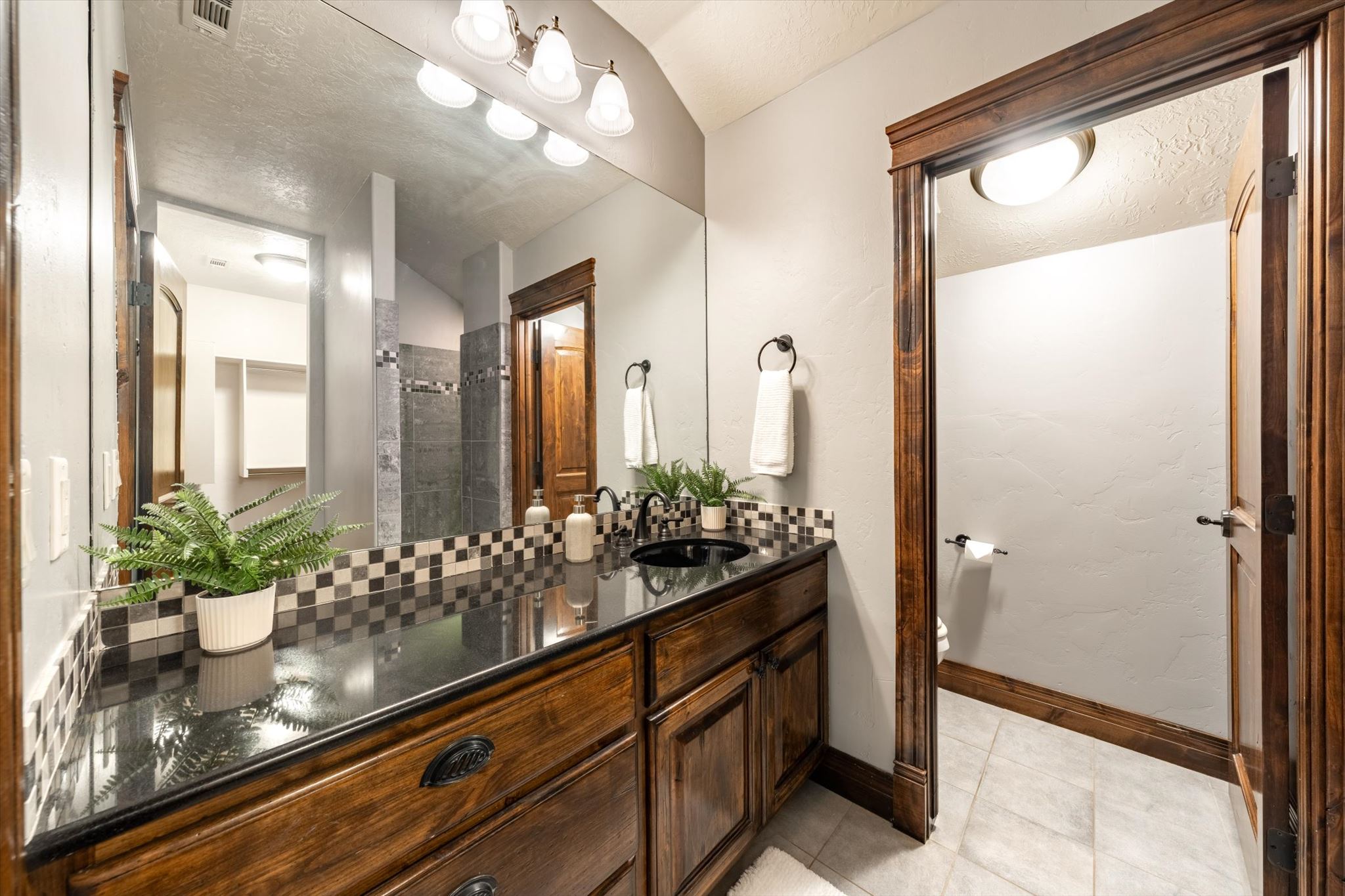 Bathroom vanity featuring a dark wood finish, black countertop, and checkerboard tile backsplash
