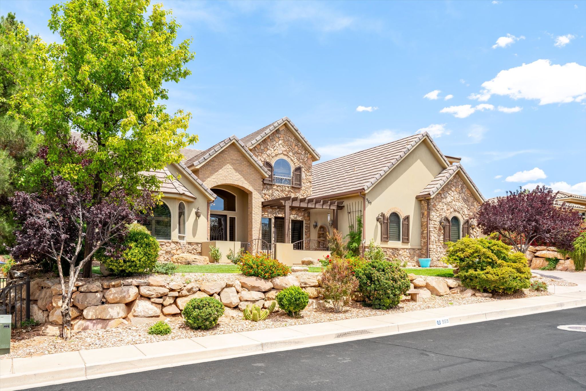 Stone and stucco exterior featuring a tile roof, arched windows with shutters, and a front entry pergola
