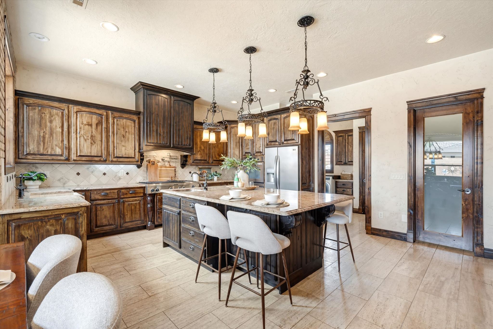 Spacious kitchen featuring an oversized island with pendant lighting, stone countertops, stainless steel appliances, wood-finish cabinetry, and tiled flooring