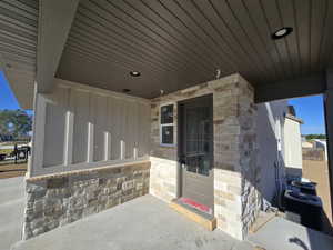 Covered patio featuring a stone veneer accent wall, board and batten siding, recessed lighting, concrete flooring, and a glass-paneled door