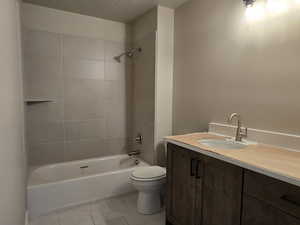 Bathroom featuring a wood-finish vanity with an undermount sink and brushed nickel faucet, a shower/tub combination with light-toned tile surround, and tile flooring