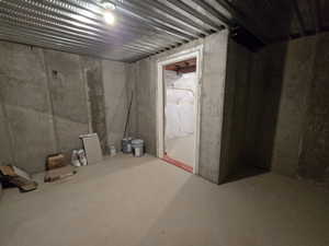 Unfinished concrete room featuring exposed metal joists and a bare bulb light fixture